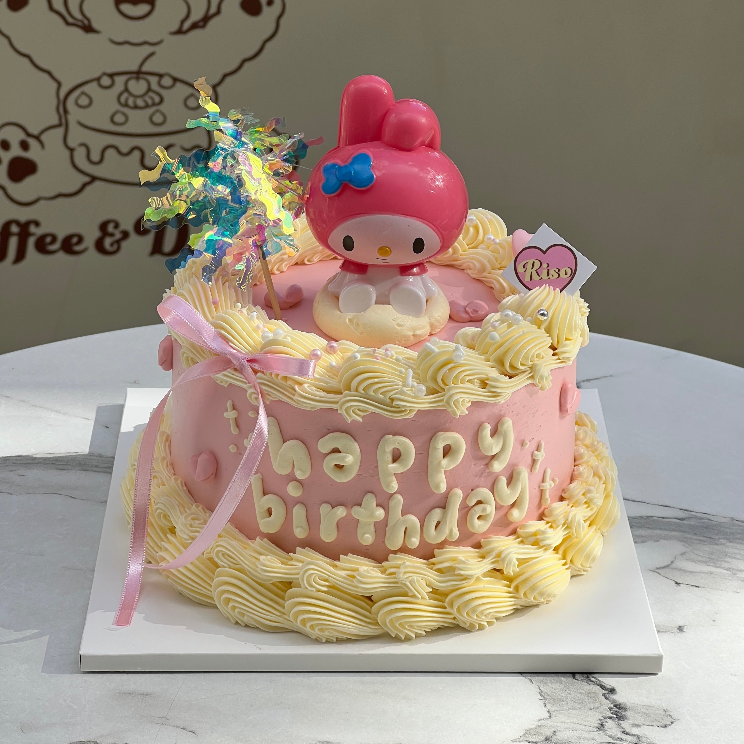 A pink birthday cake topped with a 3D My Melody figure, piped yellow frosting, and pink ribbons