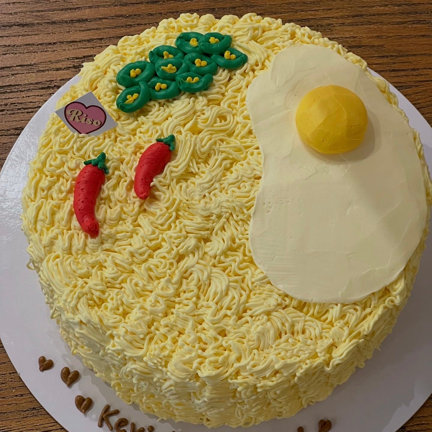 Realistic instant noodle cake made with buttercream piping, decorated with a fried egg, red chili, and vegetables — great for food-themed parties or quirky celebrations
