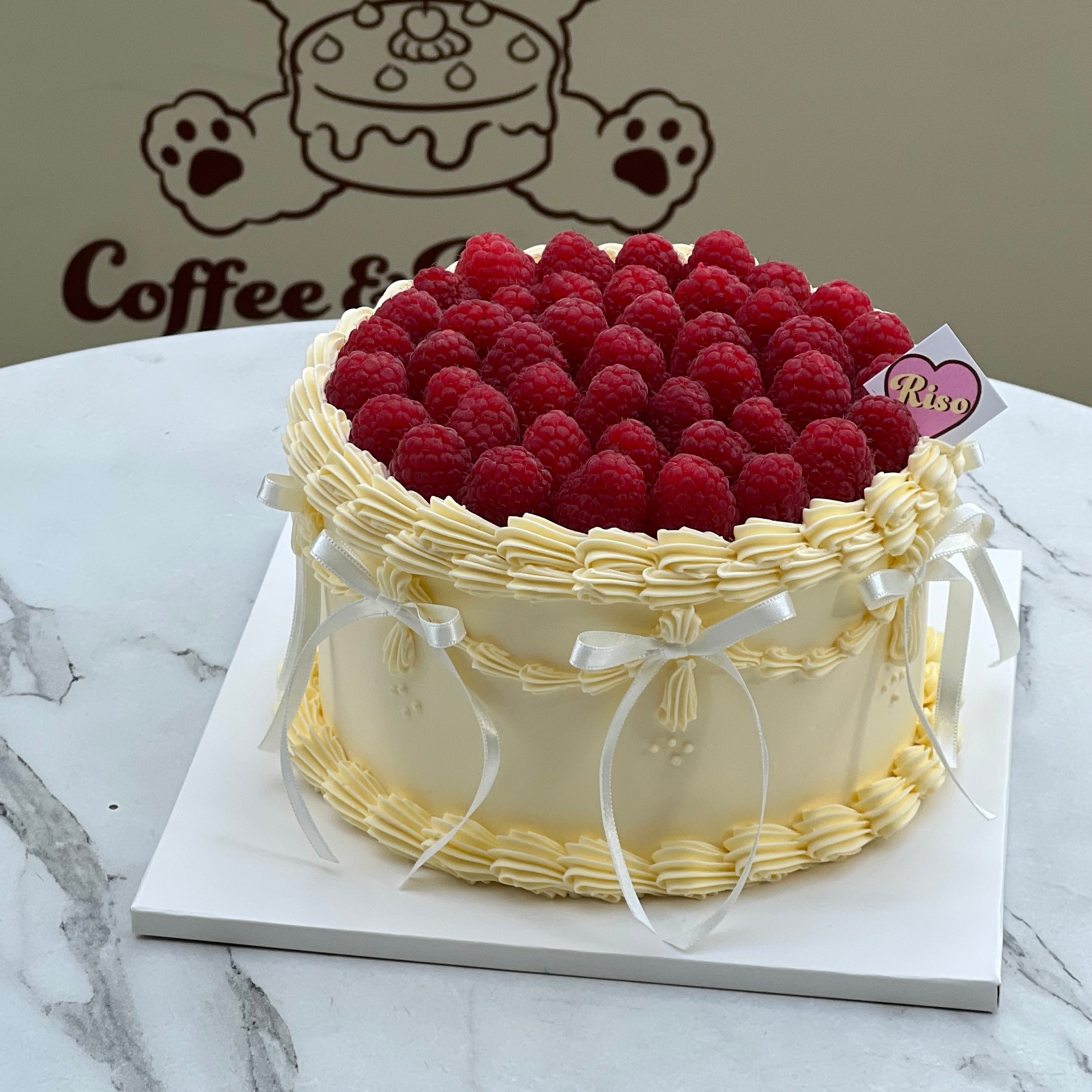 Balletcore-inspired raspberry cake with vintage-style piped cream, white ribbon bows, and a crown of juicy fresh raspberries — perfect for elegant celebrations