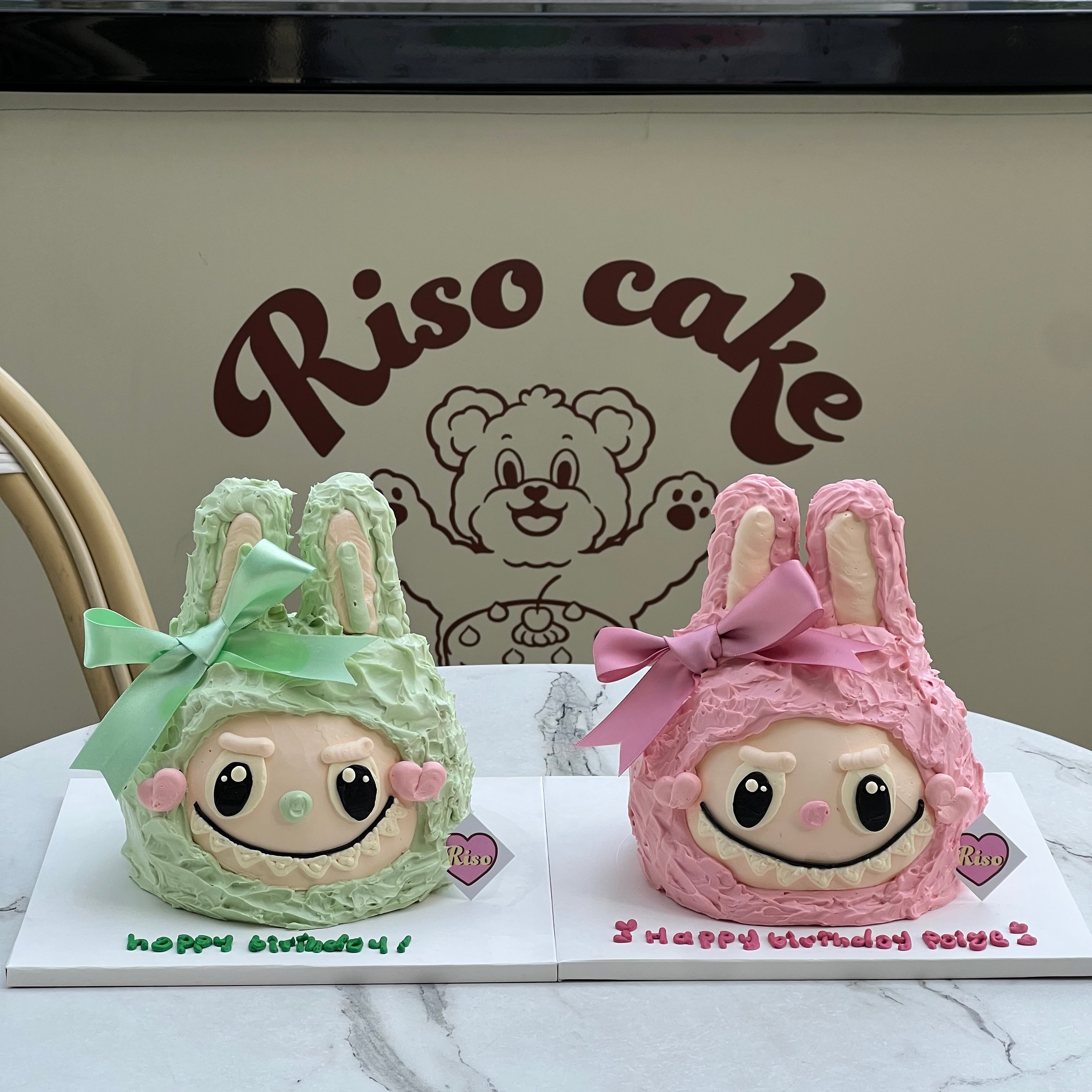 Close-up of pink Labubu cake with furry texture, big eyes, and a soft ribbon tied between two upright bunny ears