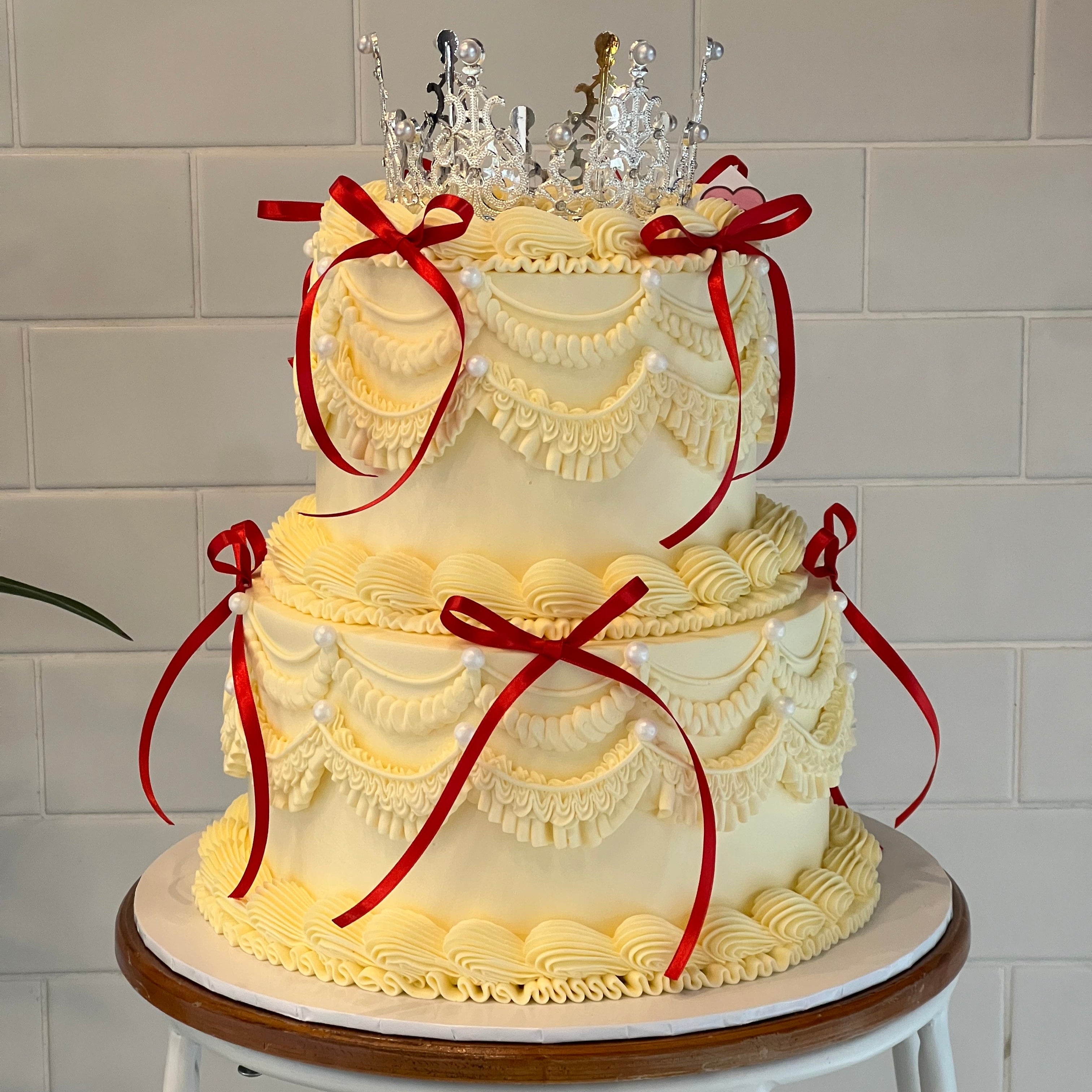 Riso Cake’s custom two-tier vintage birthday cake with crown topper, red bows, and piped cream details