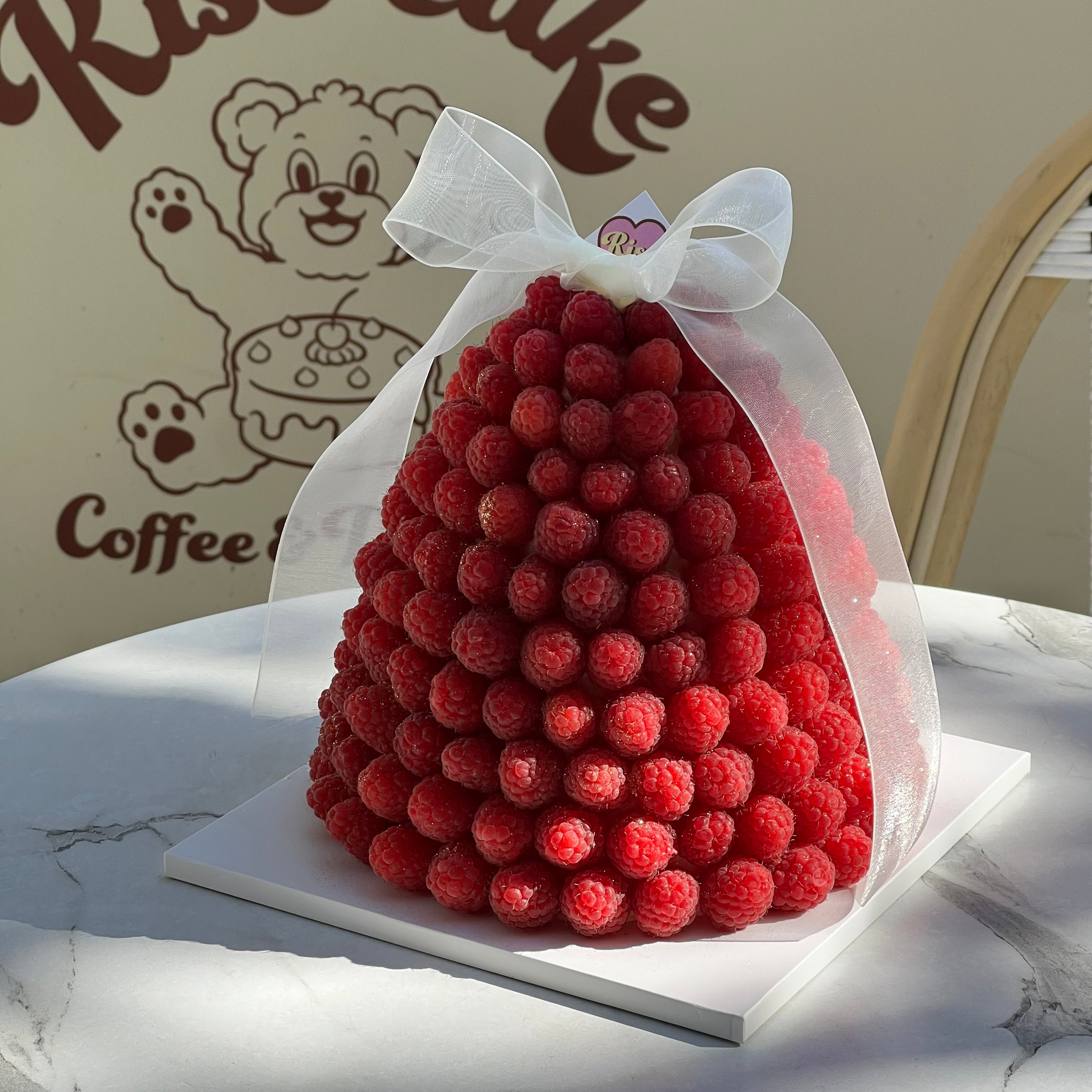 Tower-shaped raspberry cake stacked with fresh berries, wrapped with a white organza ribbon, perfect for birthdays and special events