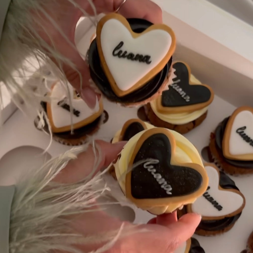 Box of cupcakes viewed from above, each topped with black and white heart cookies and piped cream