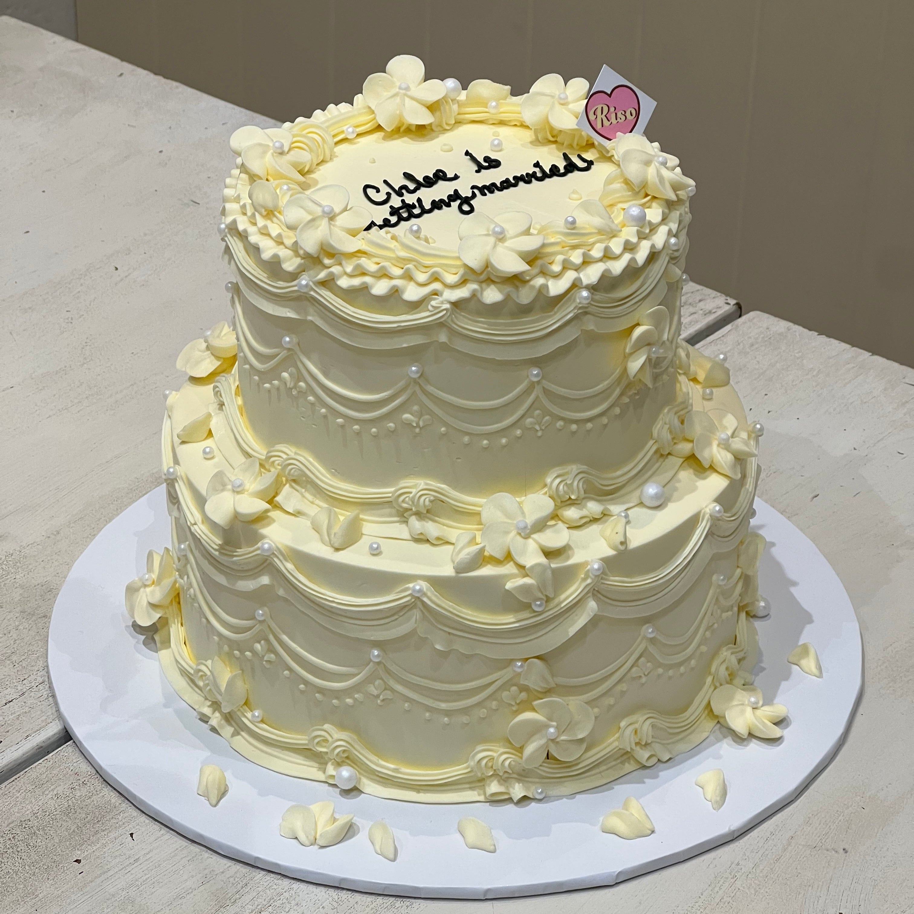 Custom engagement party cake by Riso Cake – vintage two-tier design with floral piping and pearl accents