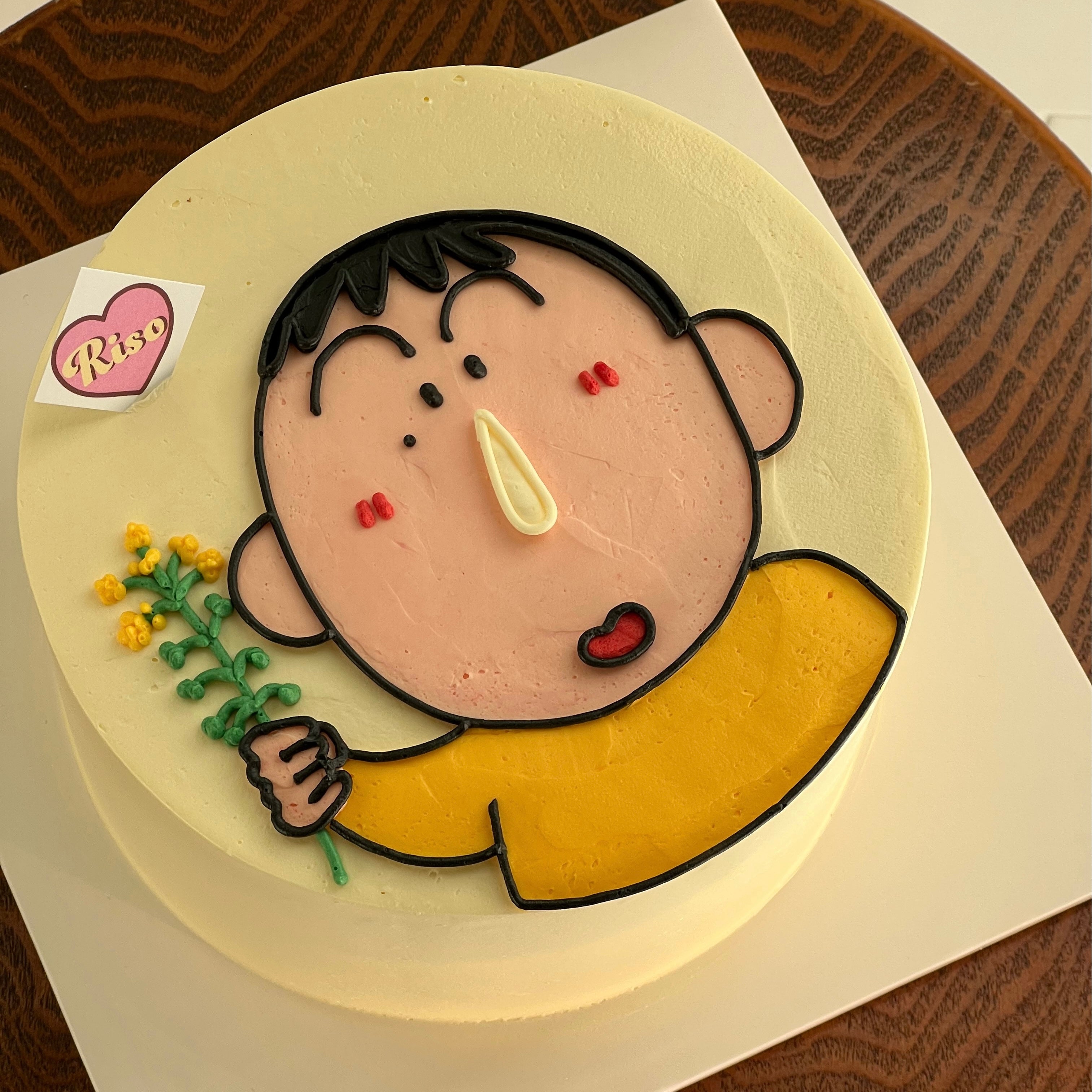 Top-down angle of a character cake showcasing Bo in yellow with blush cheeks, set against a clean round cake base
