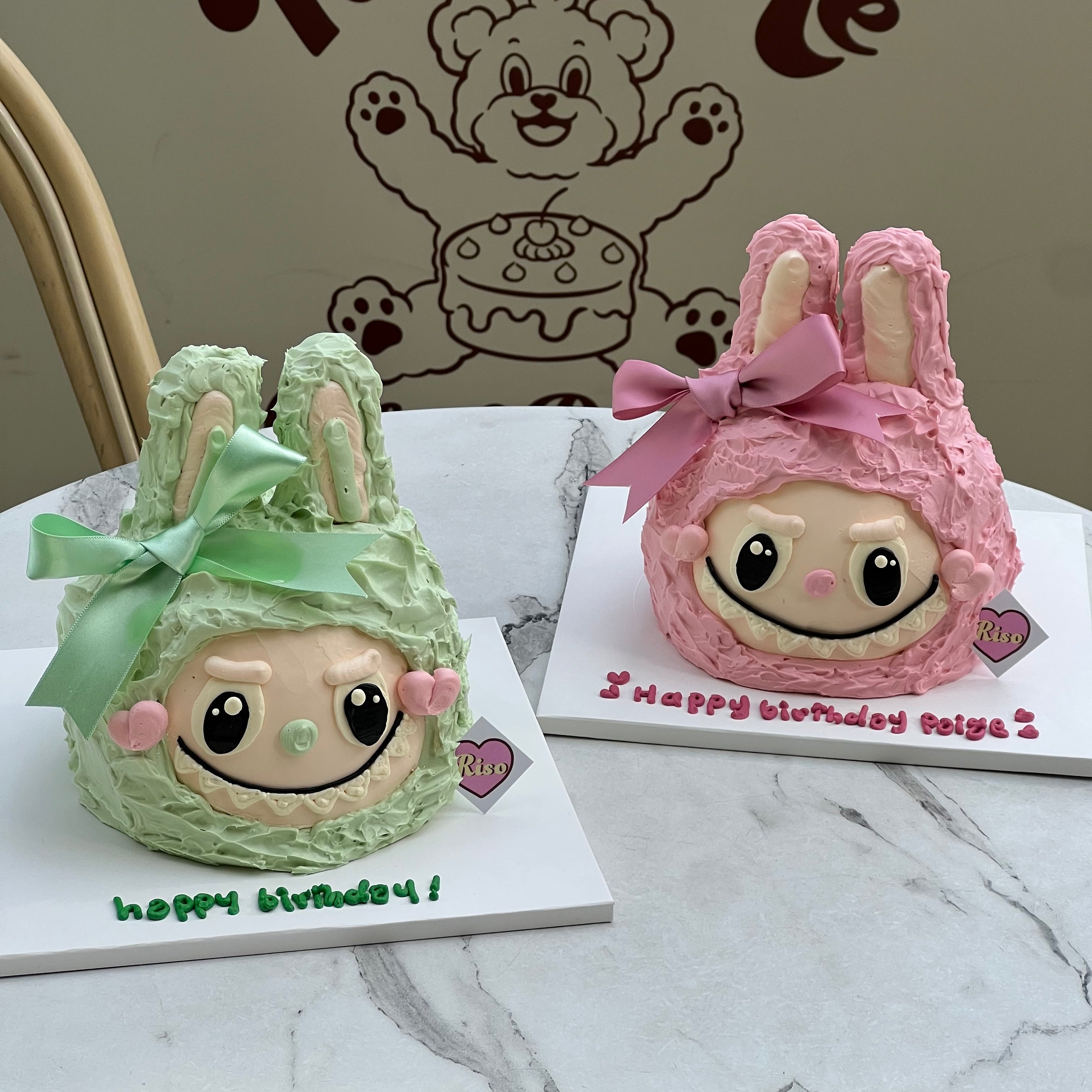 Two bunny-shaped Labubu character cakes in green and pink with big bows and detailed facial expressions