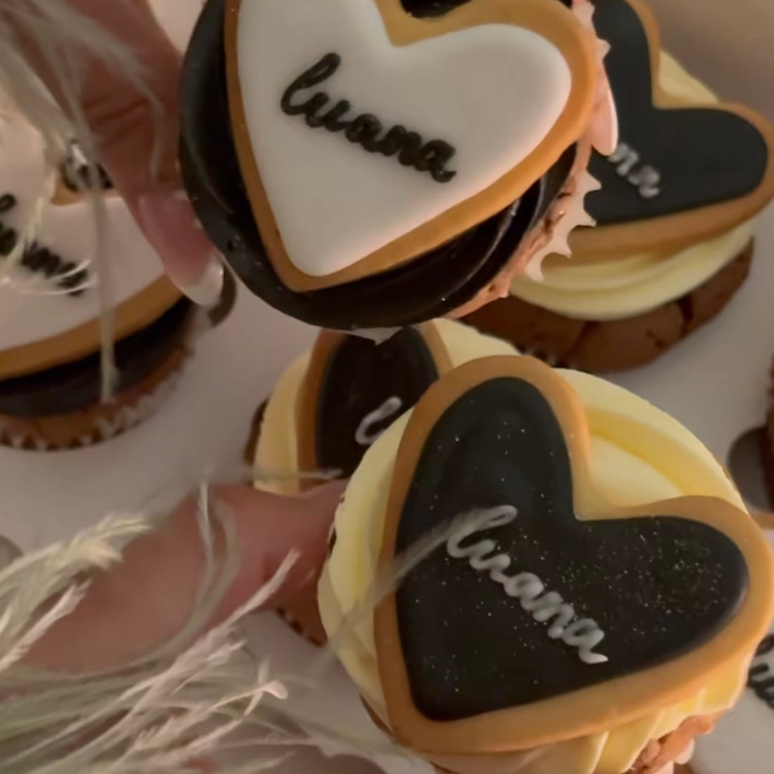 Detailed shot of cupcakes decorated with layered heart cookies and piped buttercream, featuring a name on each topper