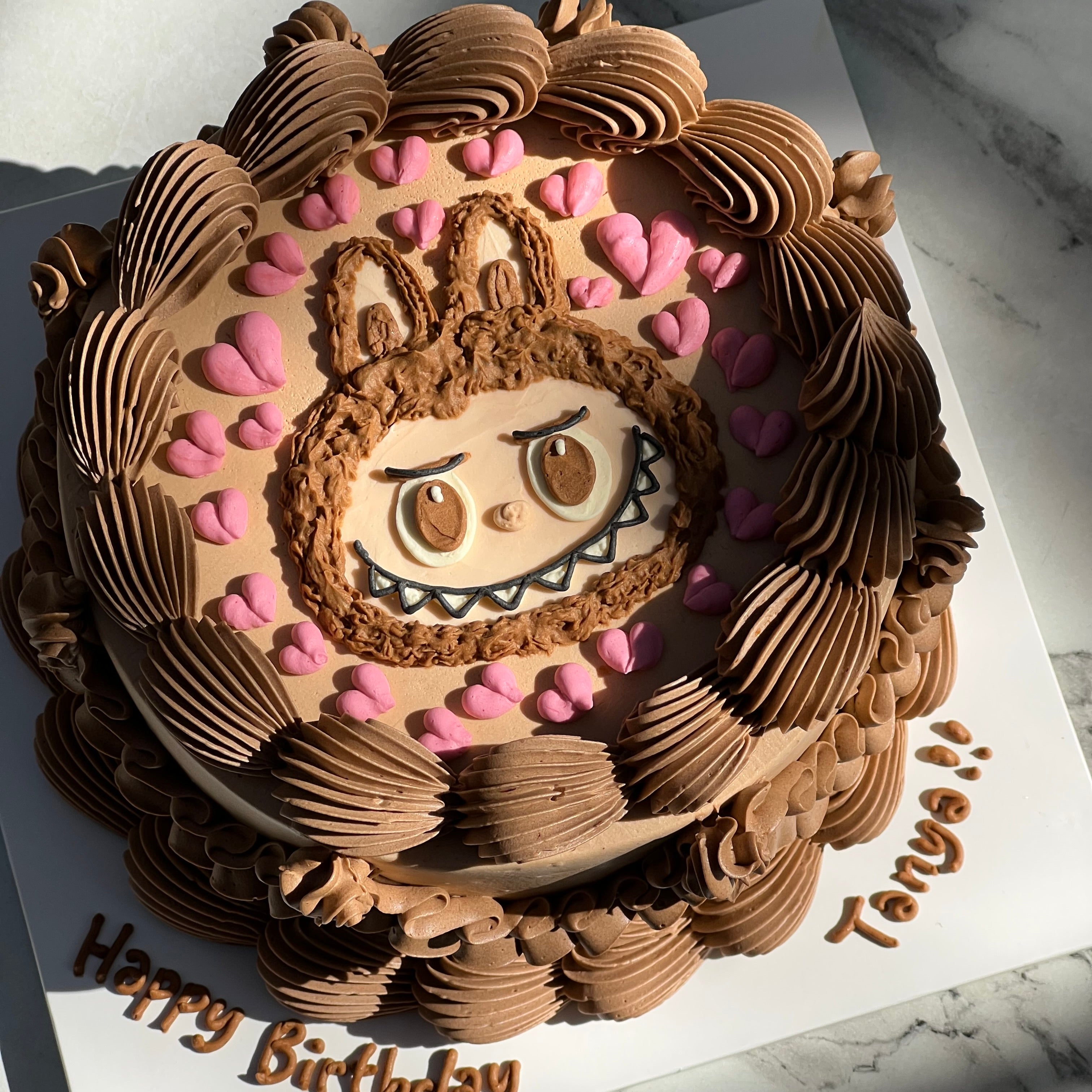 Cute Labubu birthday cake in vintage style, decorated with swirls of light brown cream and pink hearts — perfect for character cake lovers