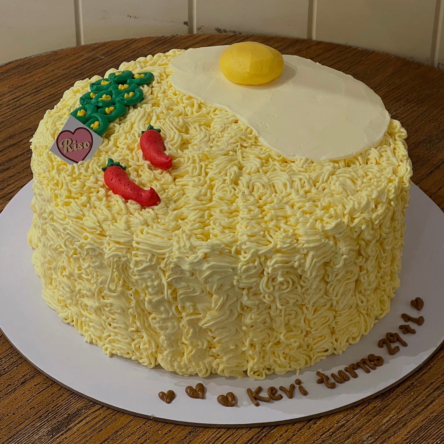 A fun ramen-inspired birthday cake topped with an icing egg, chili peppers, and green garnish