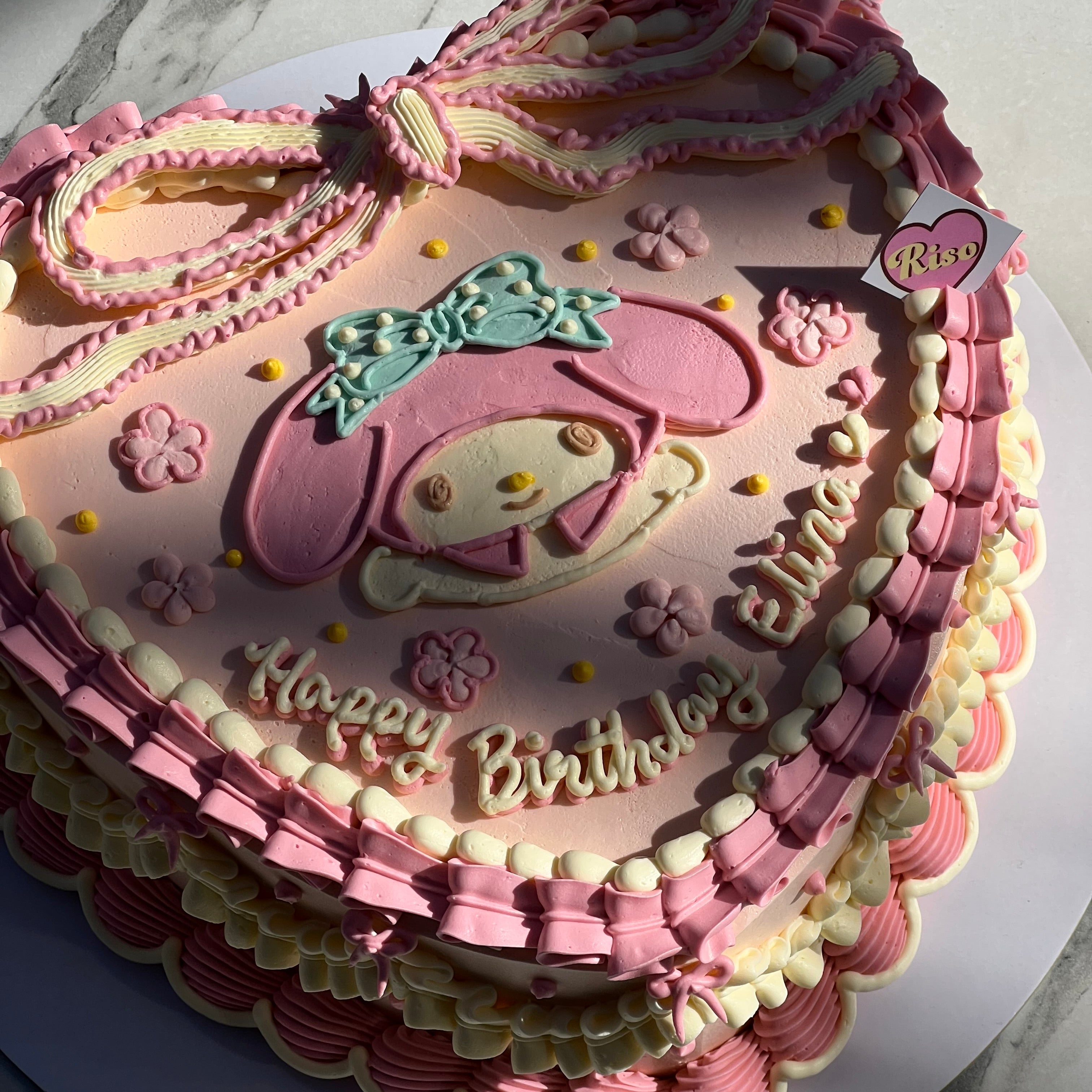 Detailed view of the piped pink ribbon, My Melody face, and delicate birthday message on a girly cake with frilled decorations