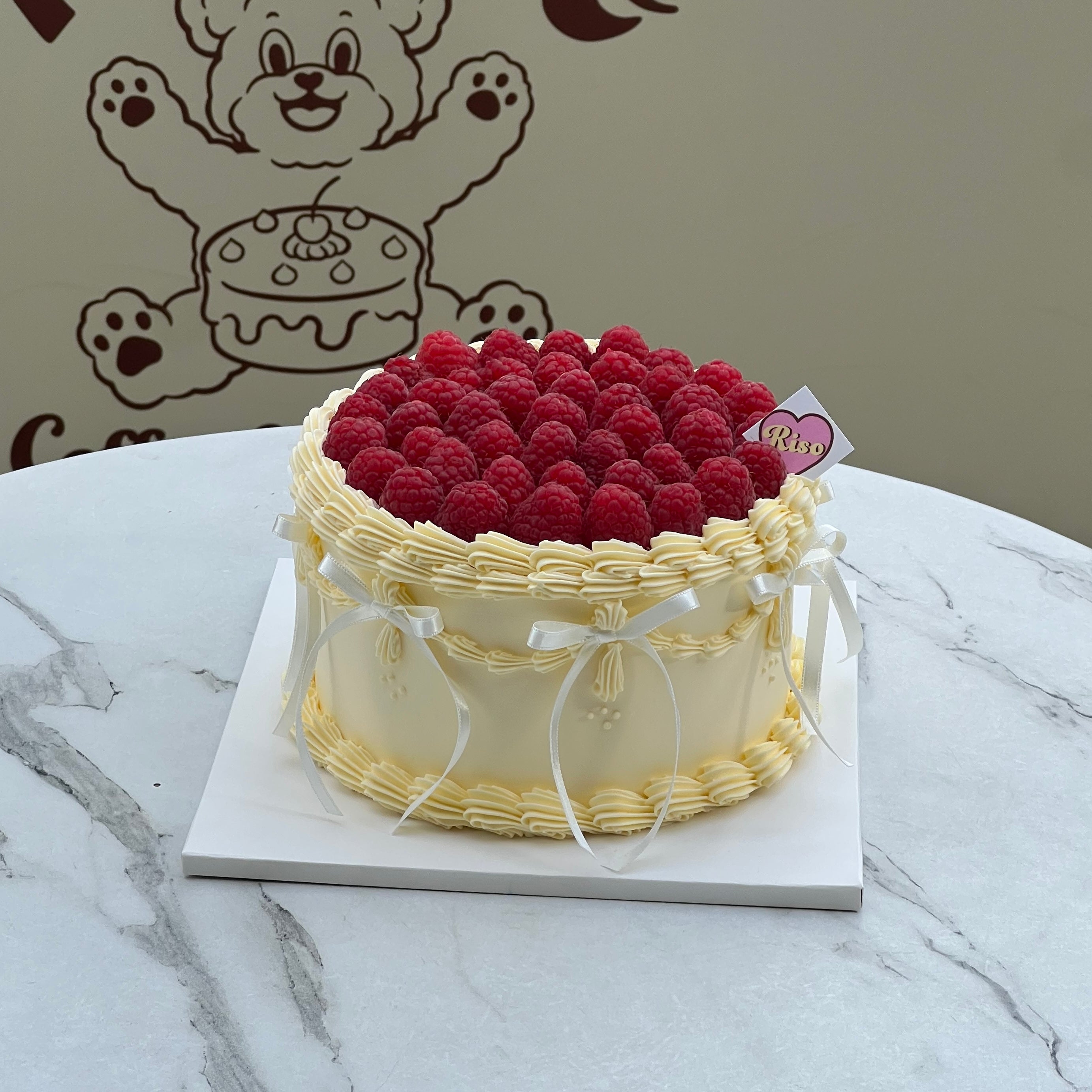 A soft and romantic cake styled in balletcore aesthetic — delicate ribbons, vintage piping, and a luscious raspberry topping create a dreamy dessert moment