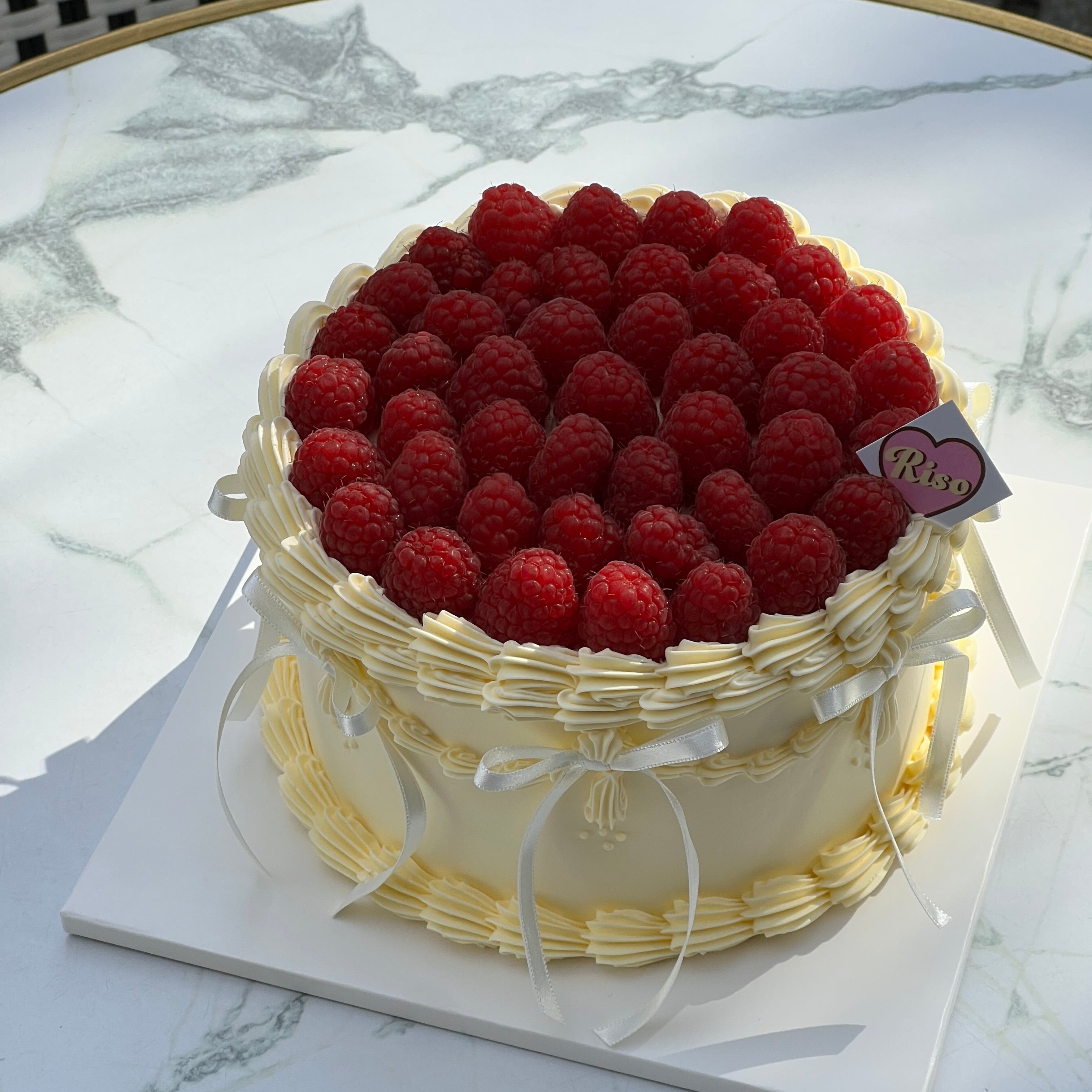 Close-up view of a raspberry-topped cake with piped cream edges and dainty white bows — classic and elegant