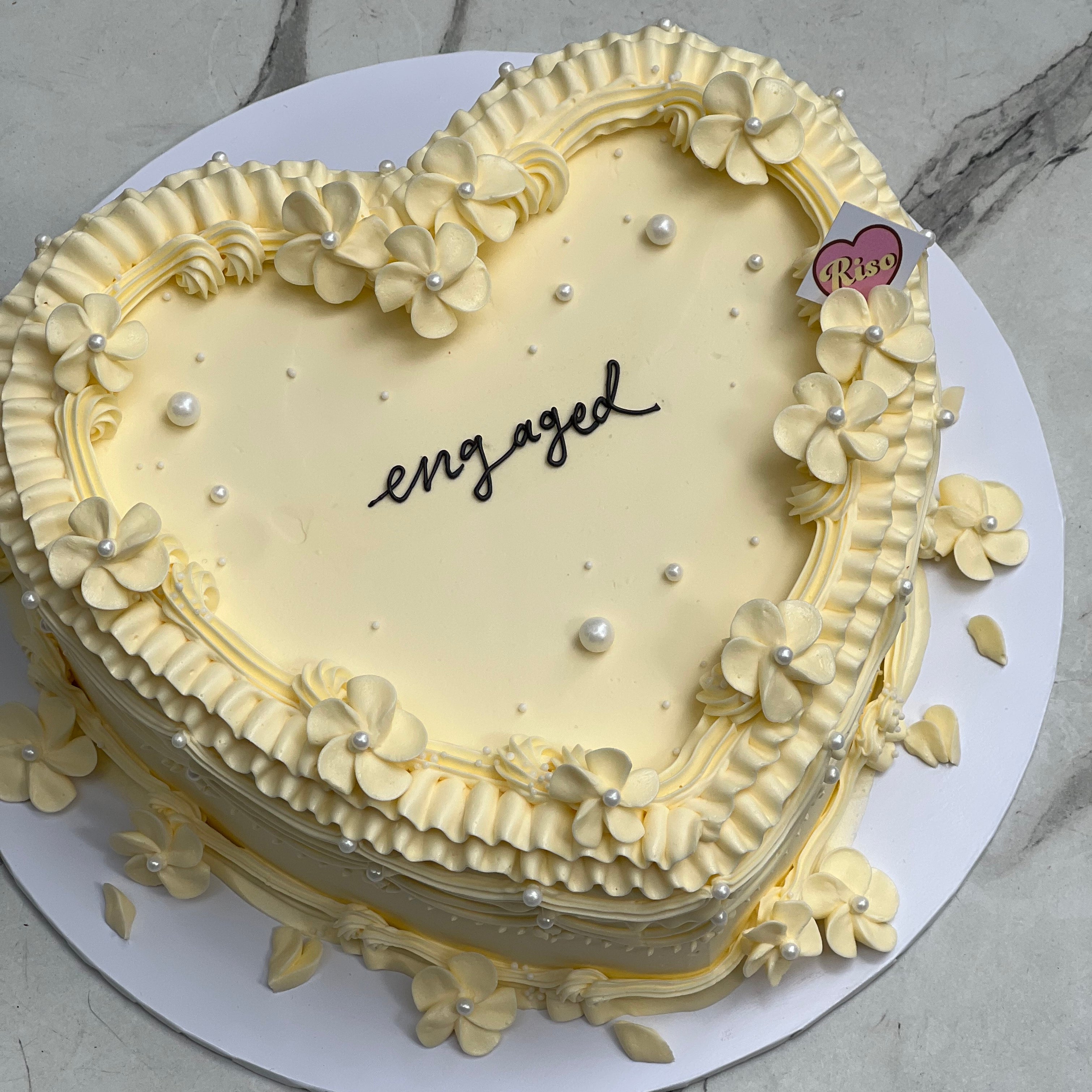 Close-up of a creamy heart cake with intricate piped blossoms and pearl accents