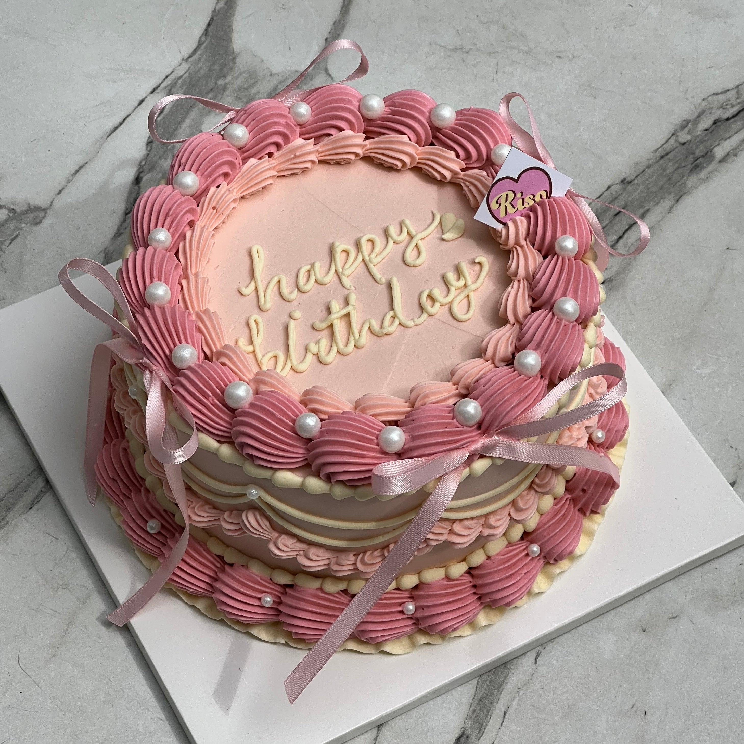 Pink vintage-style birthday cake with pearl accents and ribbon decorations
