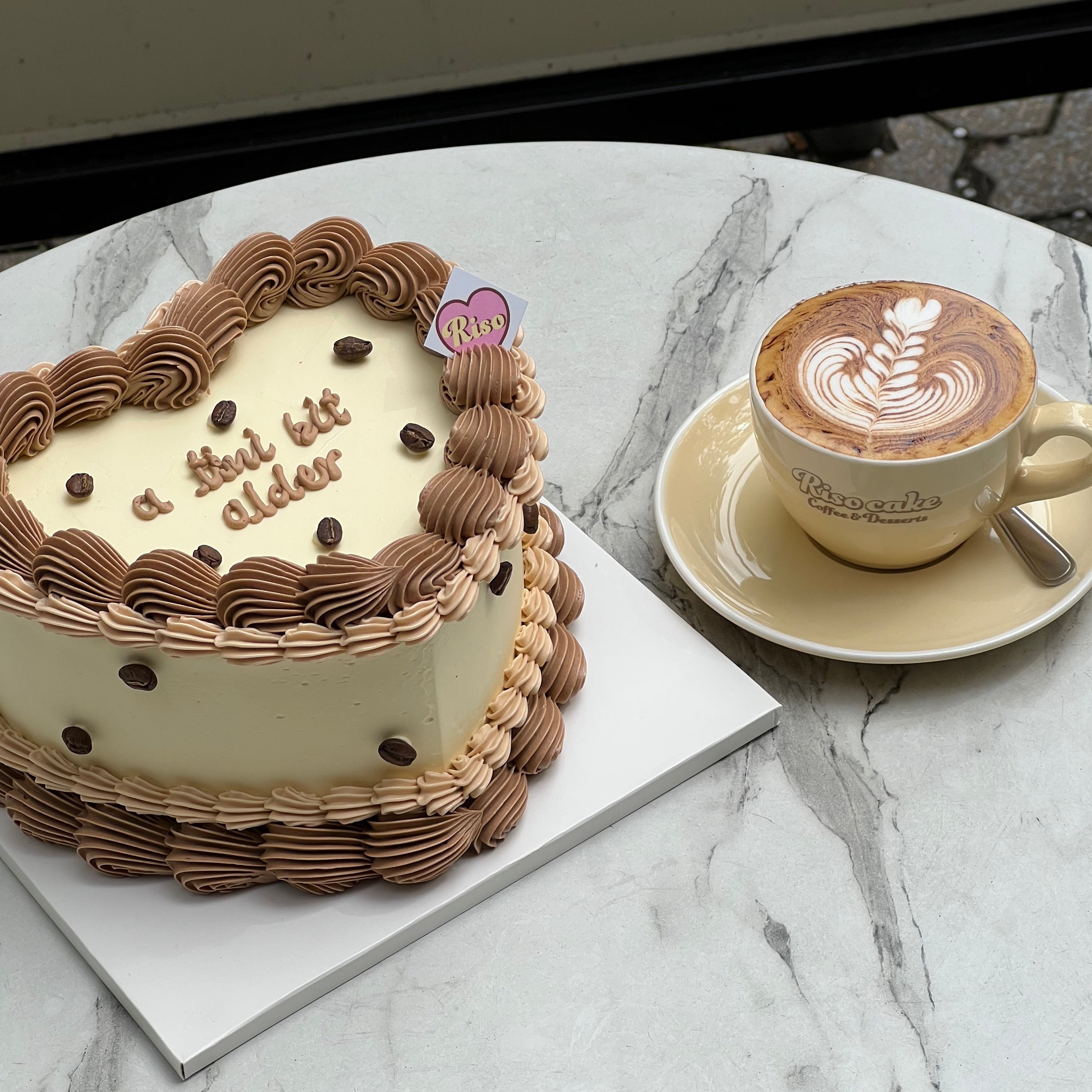Heart-shaped cake with brown and beige piping, topped with chocolate coffee bean decorations