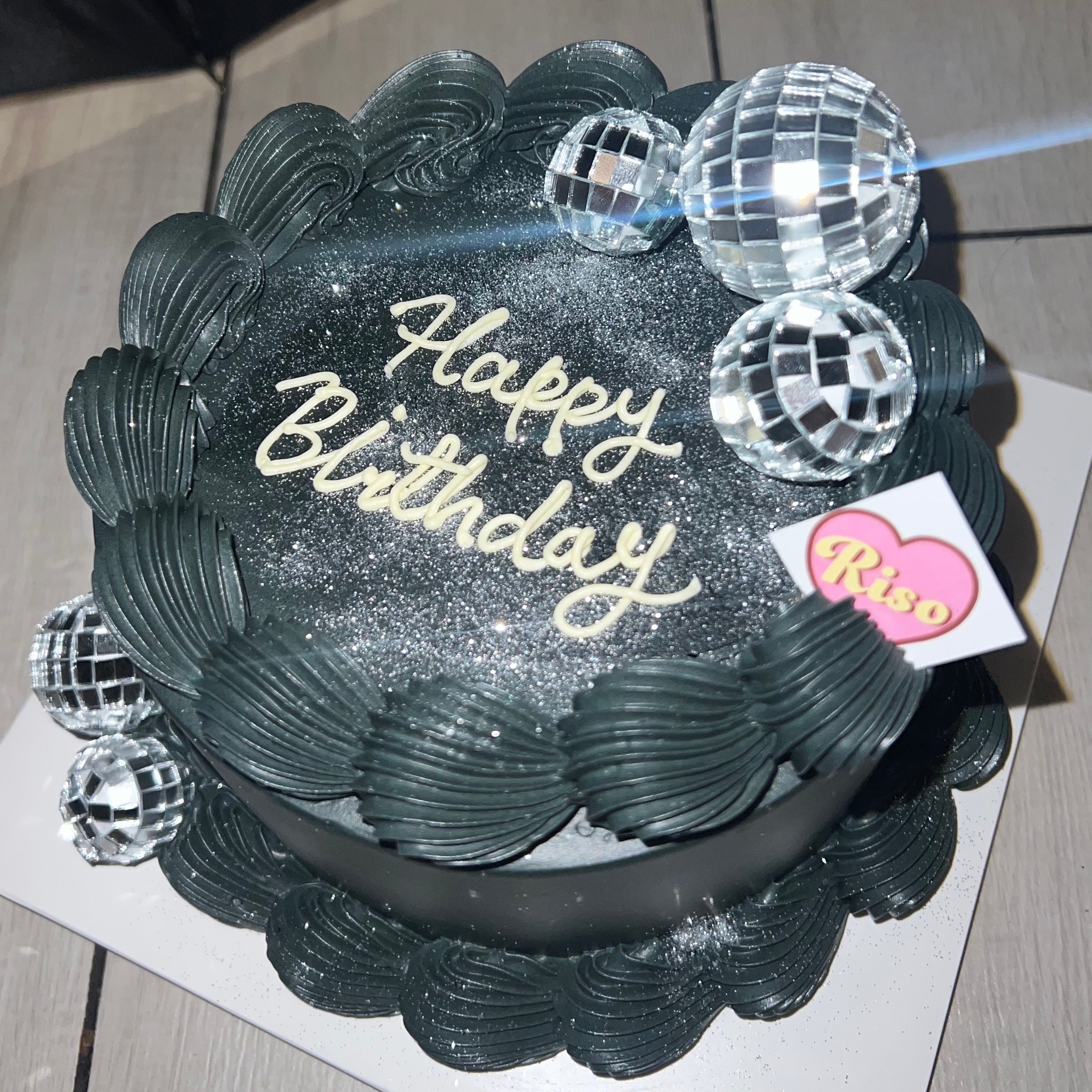 Edgy dark cake topped with mirror ball decorations, shimmering edible glitter, and bold piping