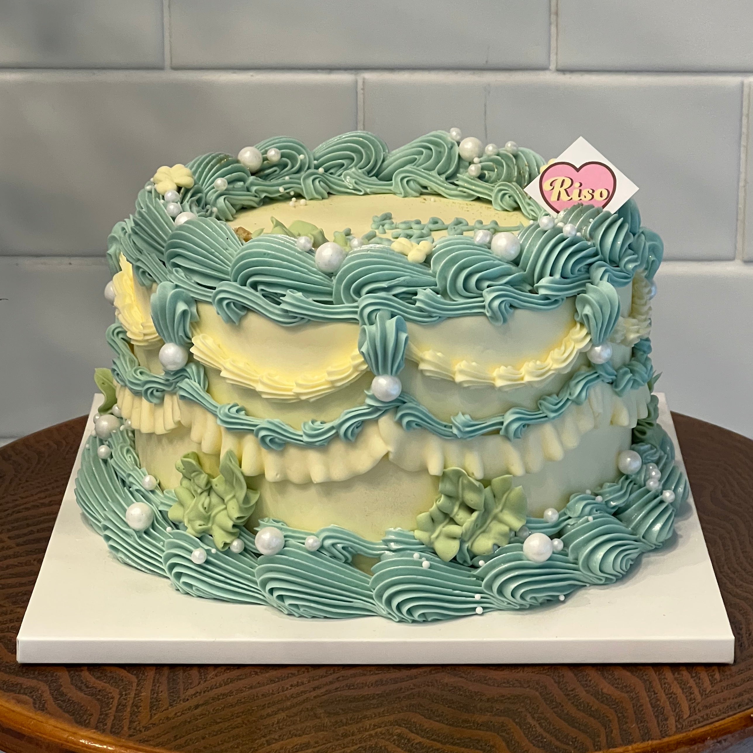 Soft cream and teal piping swirls, scattered pearls, and floral details on a vintage-style layer cake