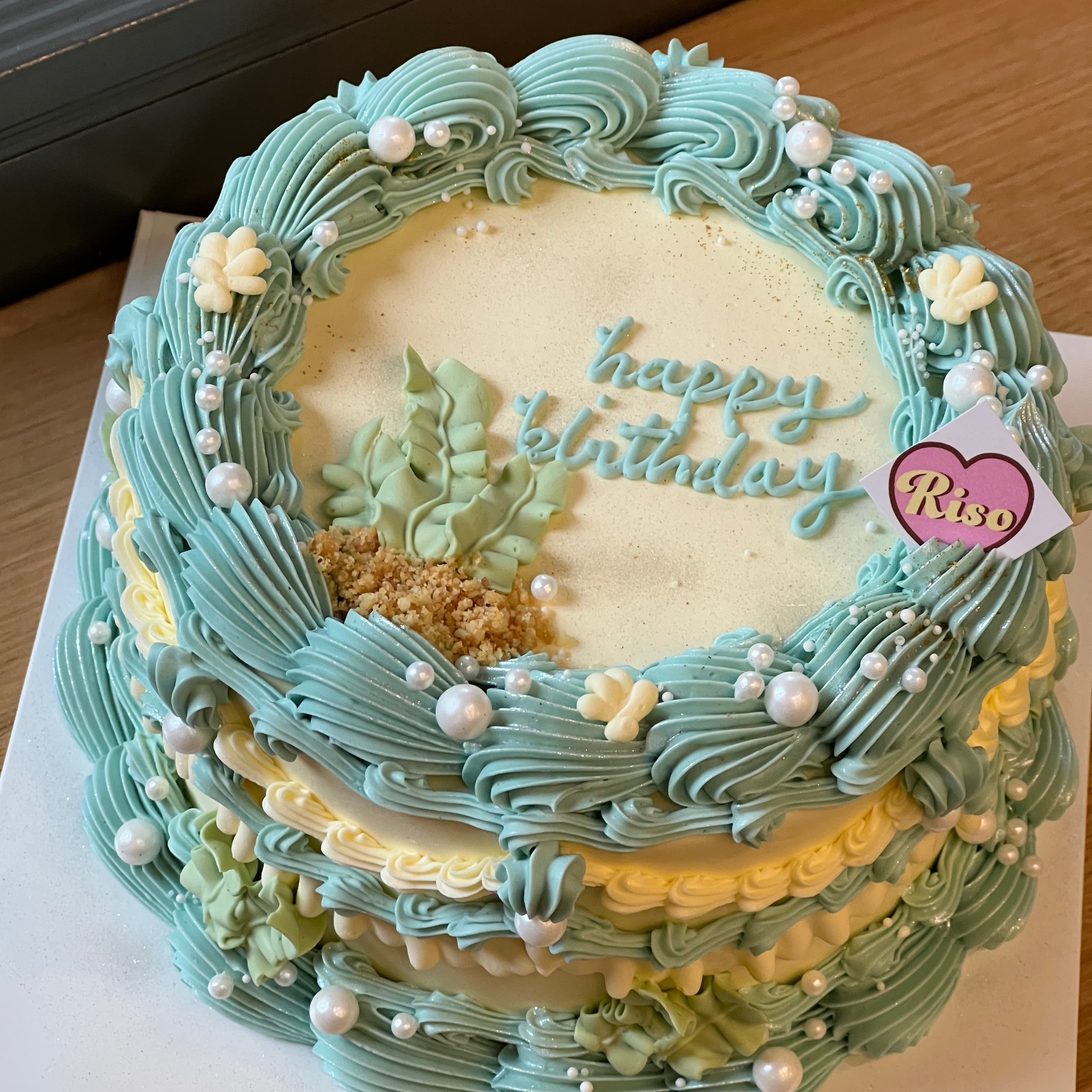 Overhead view of an ocean-themed cake with detailed piping and “Happy Birthday” lettering in seafoam green