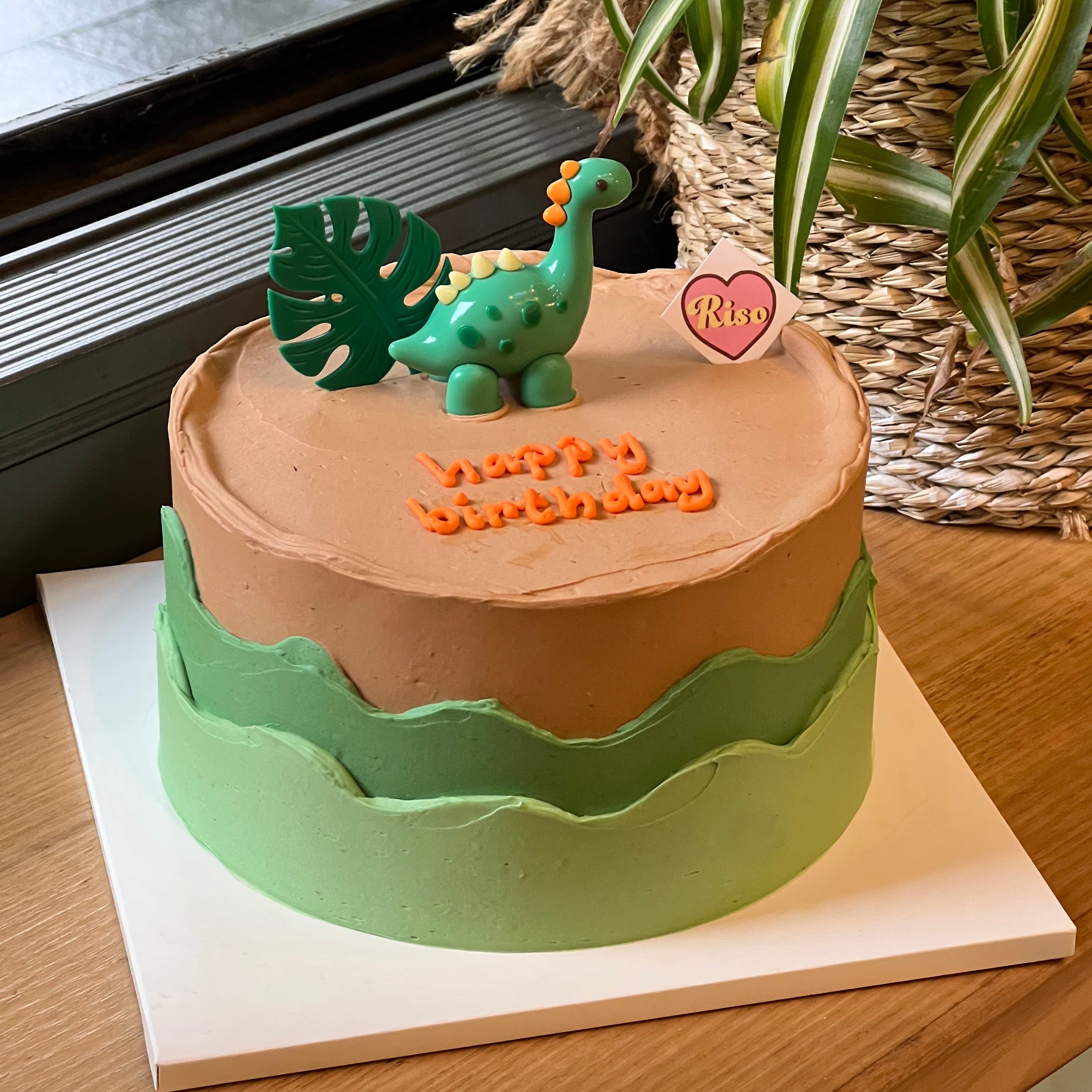 Cute dinosaur birthday cake with green forest-style frosting and playful dino figurine
