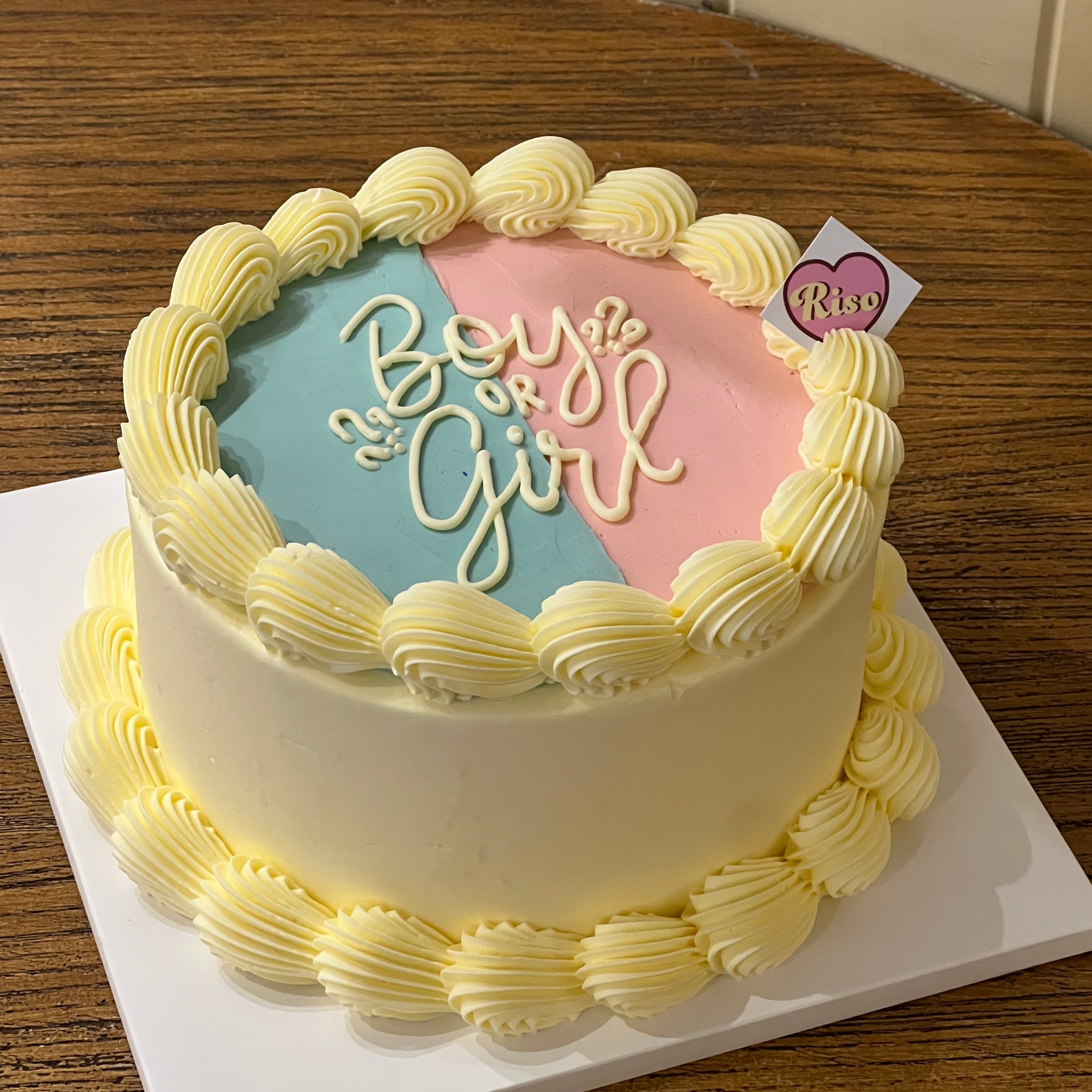 Round cake with “Boy or Girl” lettering on pink and blue split icing