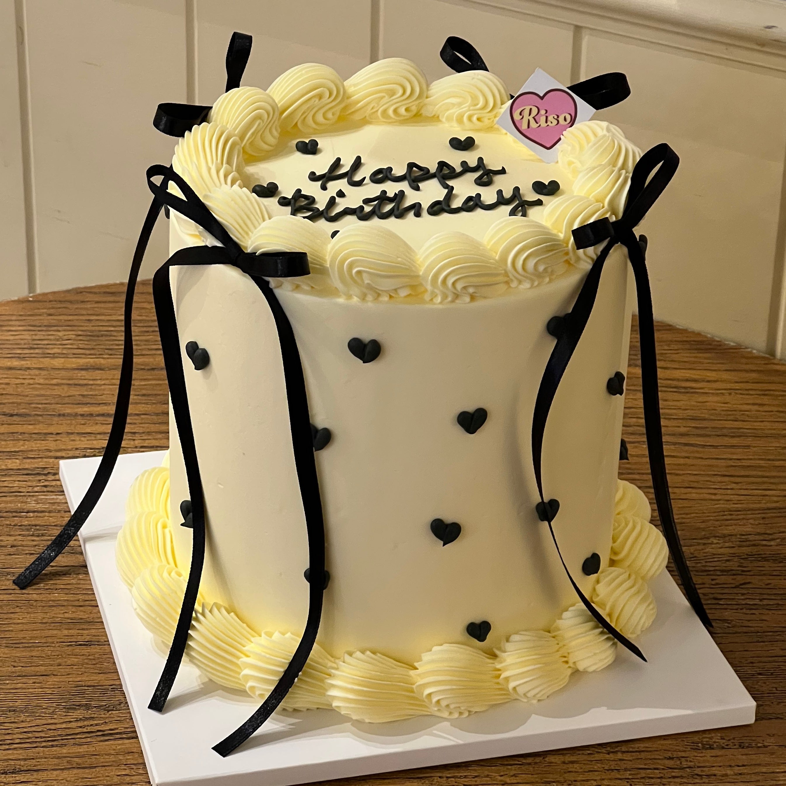 Tall vanilla cream cake with black heart decorations and black ribbon bows