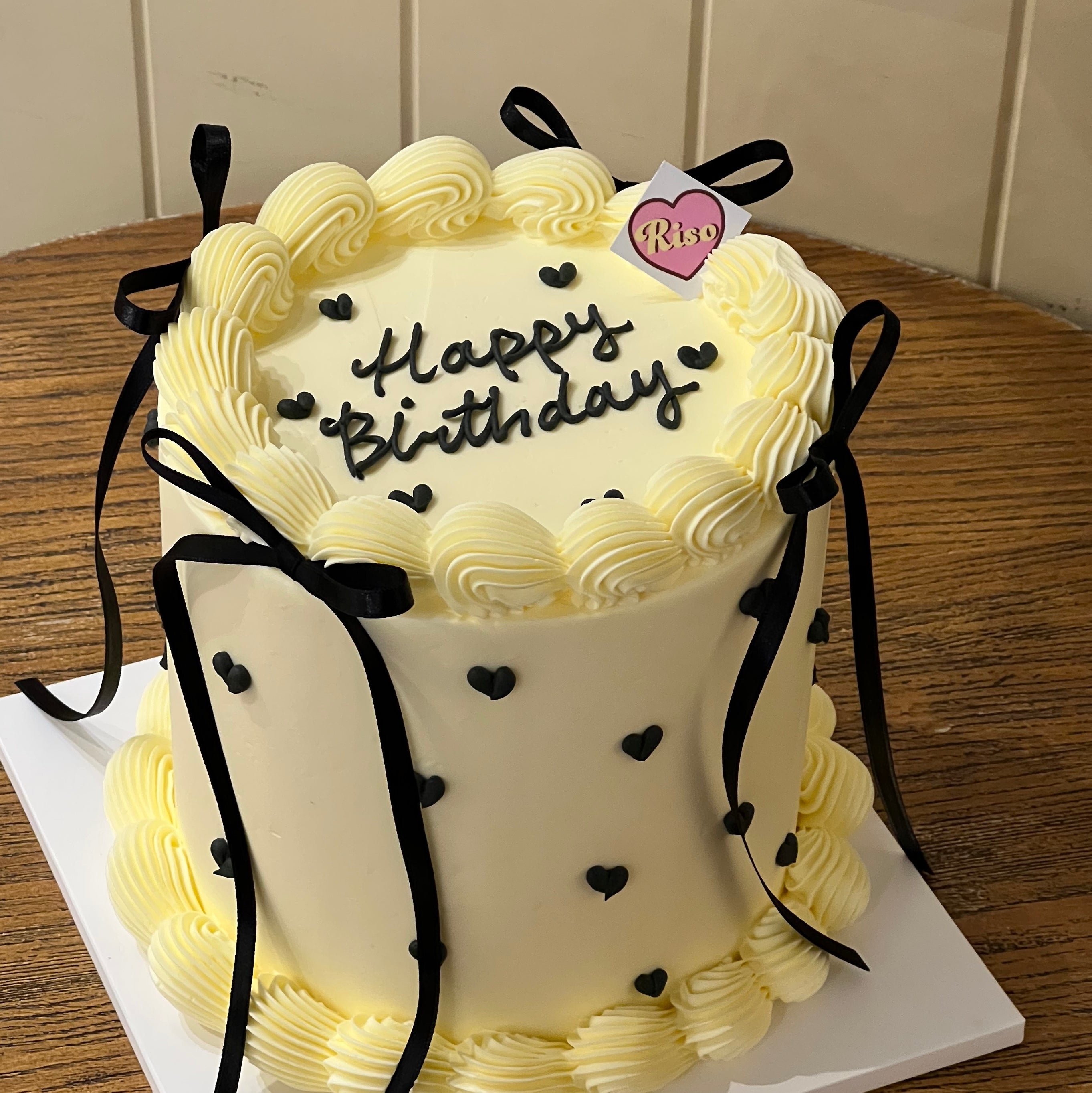 Black ribbon bows and mini hearts stand out on soft vanilla buttercream swirls