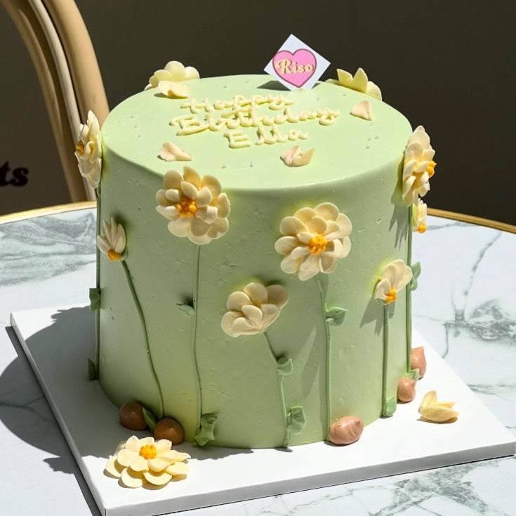 Round birthday cake with hand-piped white daisies on soft green frosting