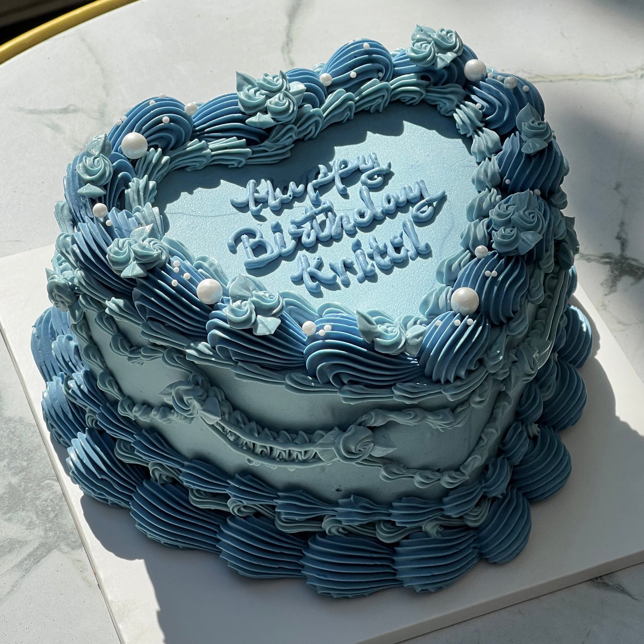 Elegant vintage-style birthday cake with double heart-shaped layers, intricate blue buttercream piping, and pearl accents, perfect for a retro celebration