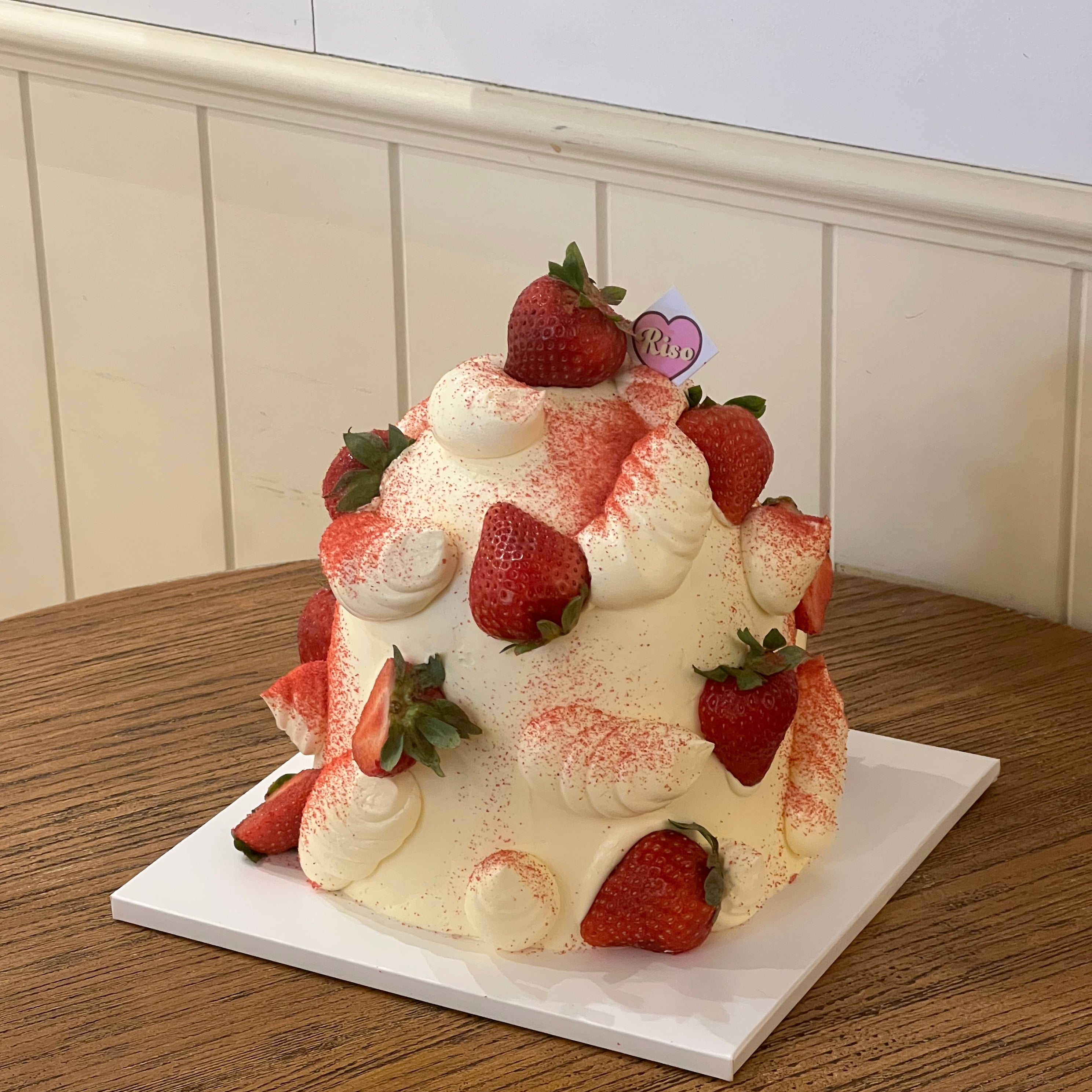 A whimsical cream-covered cake topped with juicy strawberries and soft dusting of pink powder, capturing sweet and dreamy vibes