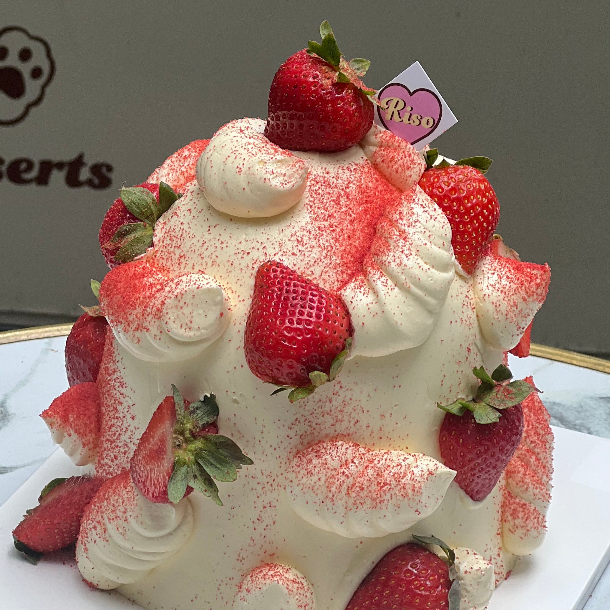Close-up of a whipped cream dome cake adorned with vibrant red strawberries and piped swirls, giving a fluffy and luscious finish