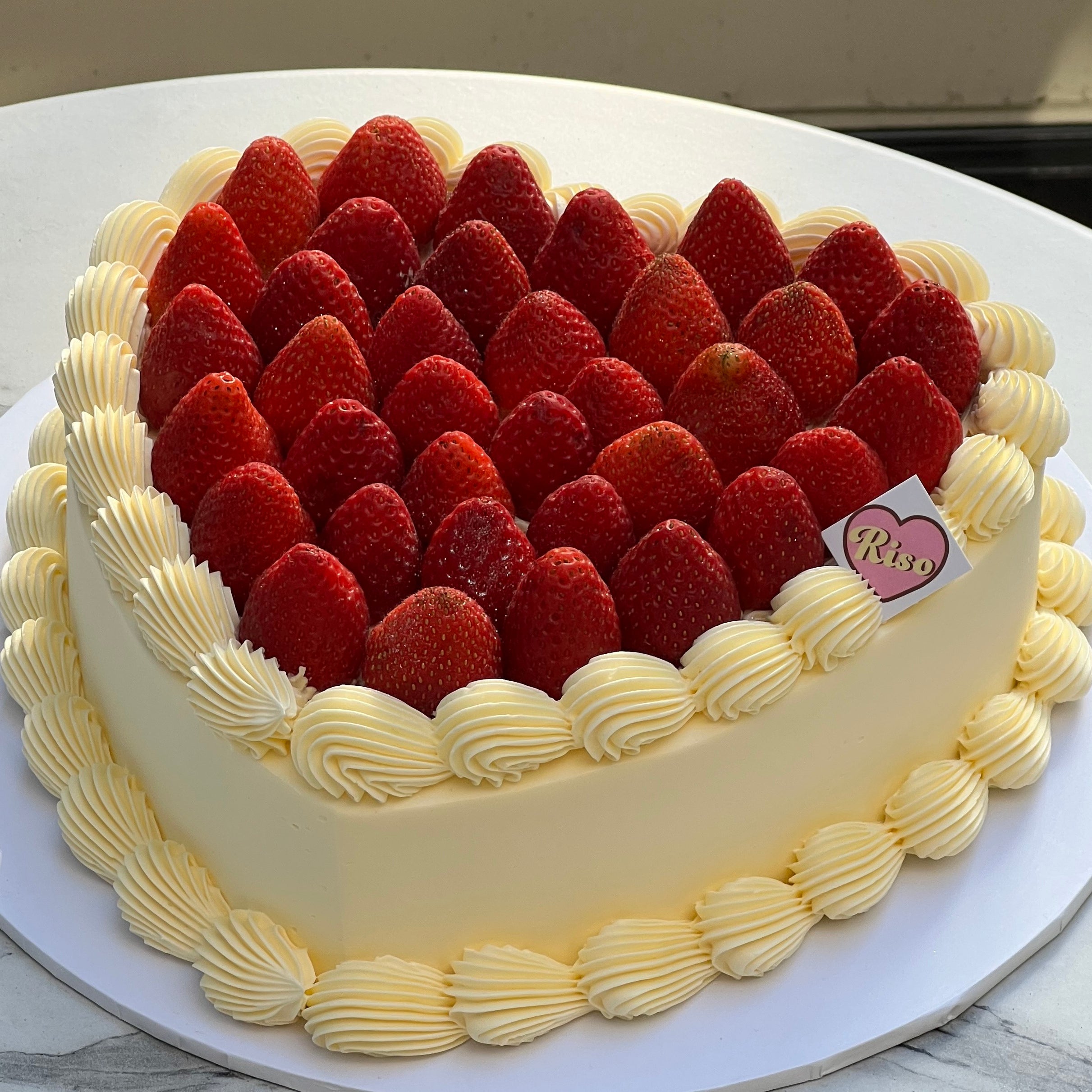 Close-up of the cake’s edge showing delicate whipped cream piping and glossy strawberries arranged in a neat heart pattern