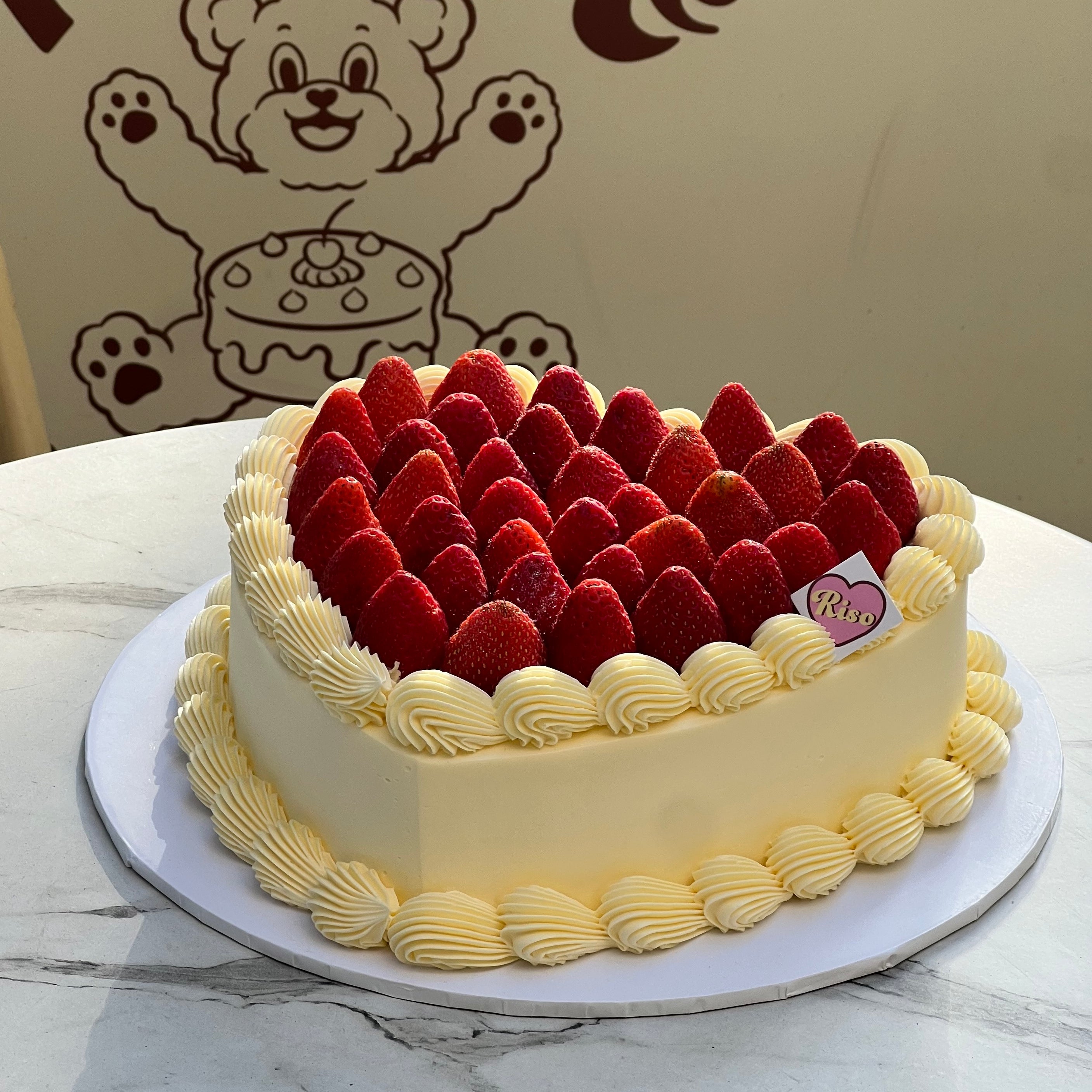 Heart-shaped large cake topped with whole strawberries and piped cream swirls around the edge