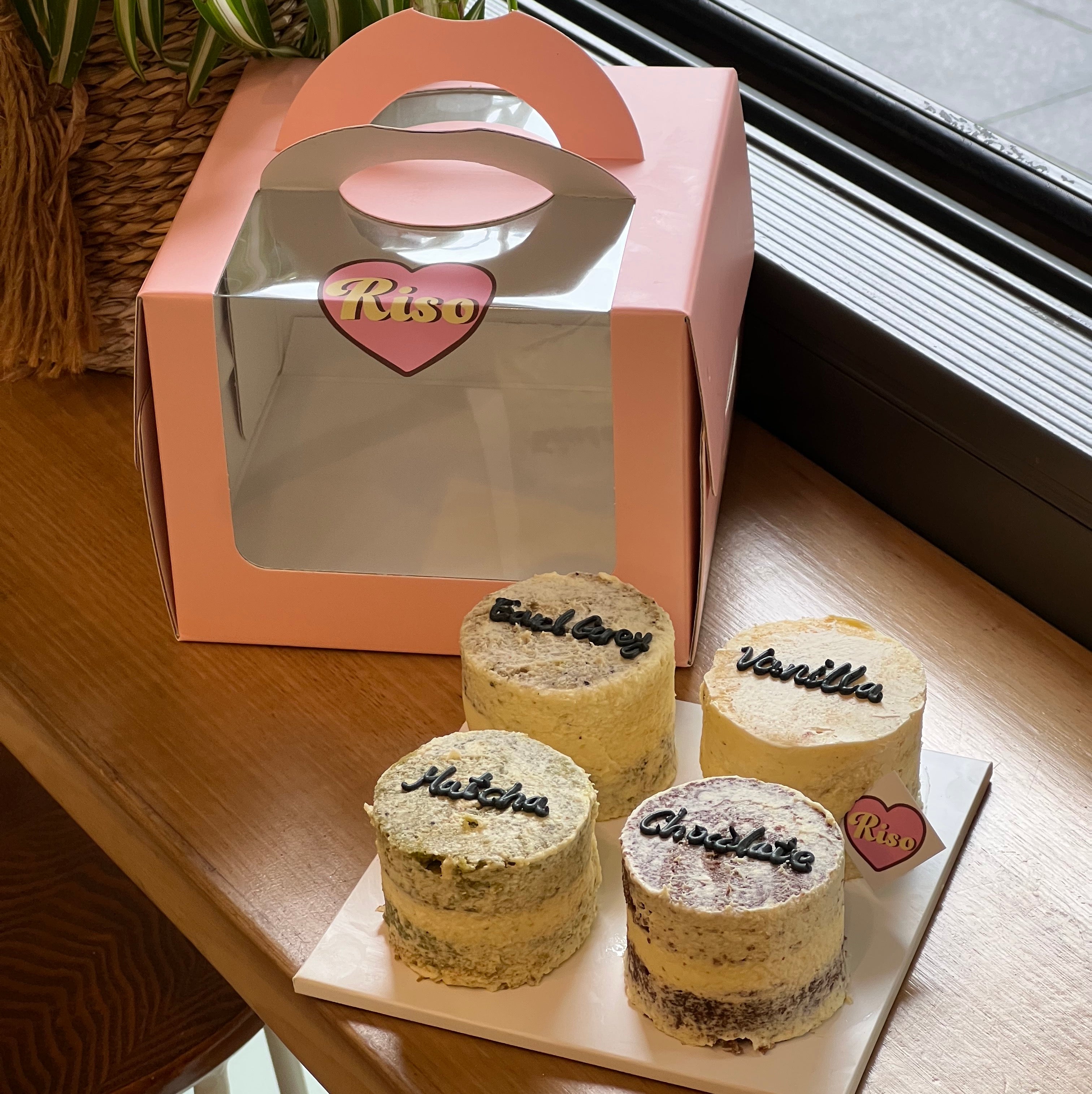 Cute and cozy cake sampler box with four rustic-style mini cakes and a pastel pink carry box, perfect for flavor testing or gifting