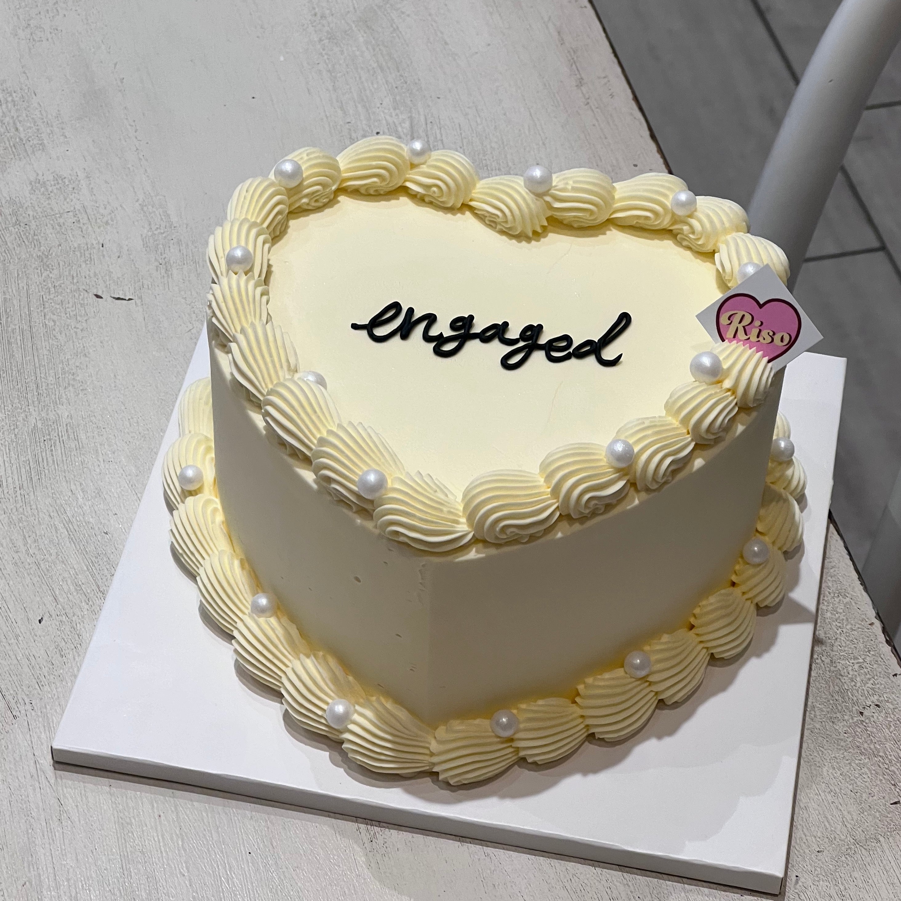 Heart-shaped cream cake with piped pearl decorations and “engaged” lettering on top
