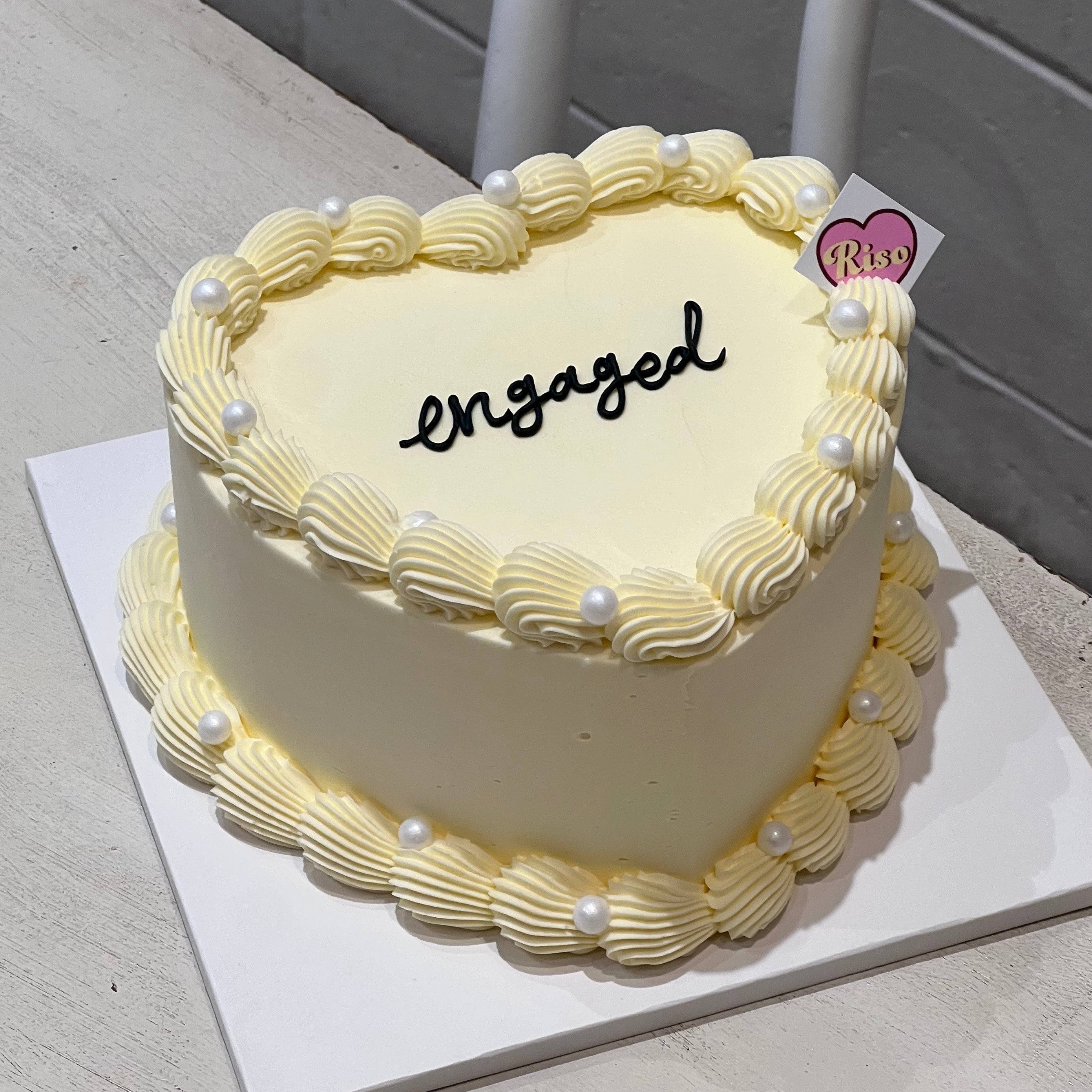 Minimalist heart-shaped engagement cake with elegant piped pearls and black script lettering, perfect for engagement parties or wedding proposals