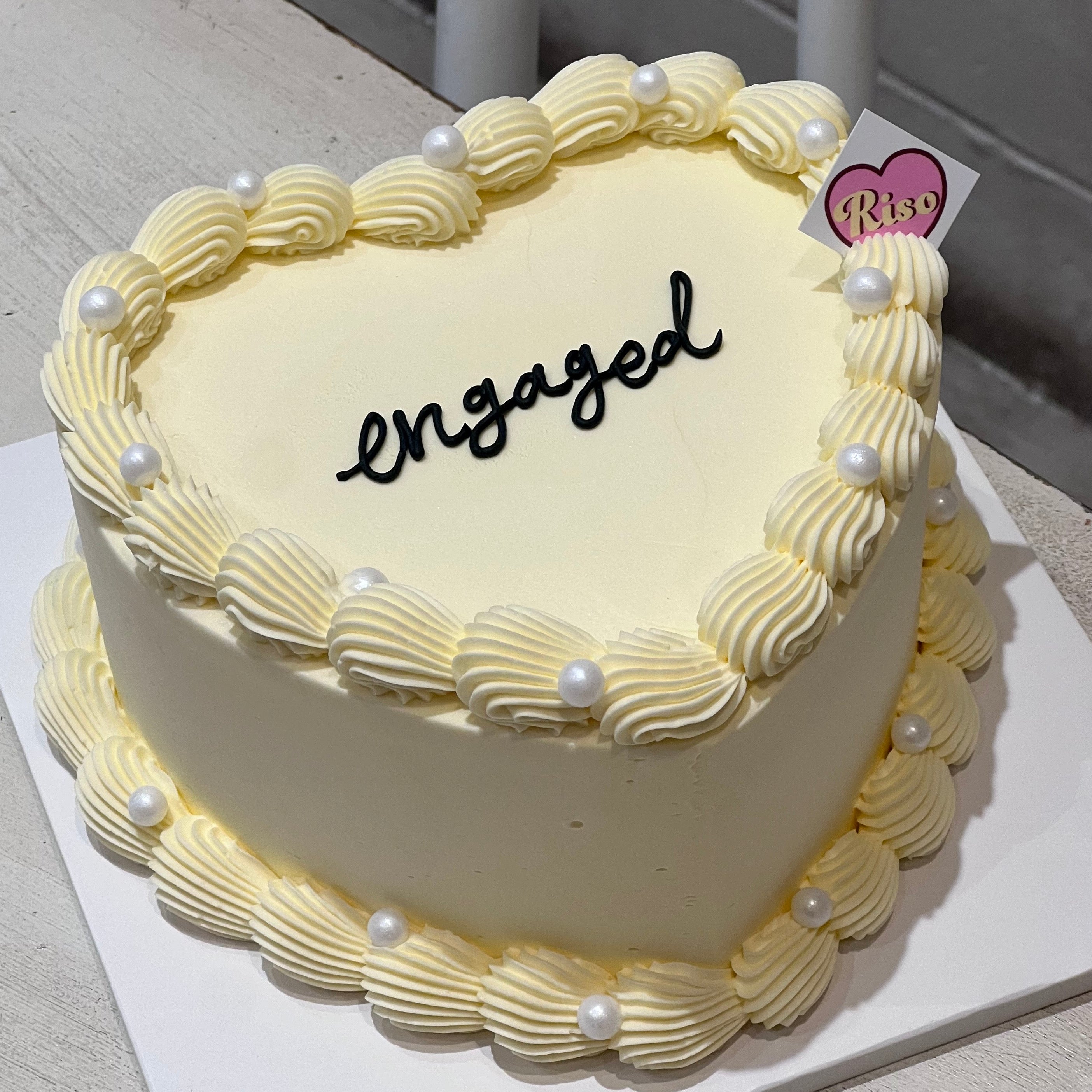 A soft and romantic heart-shaped cake adorned with white cream pearls and delicate piping, ideal for modern engagement celebrations