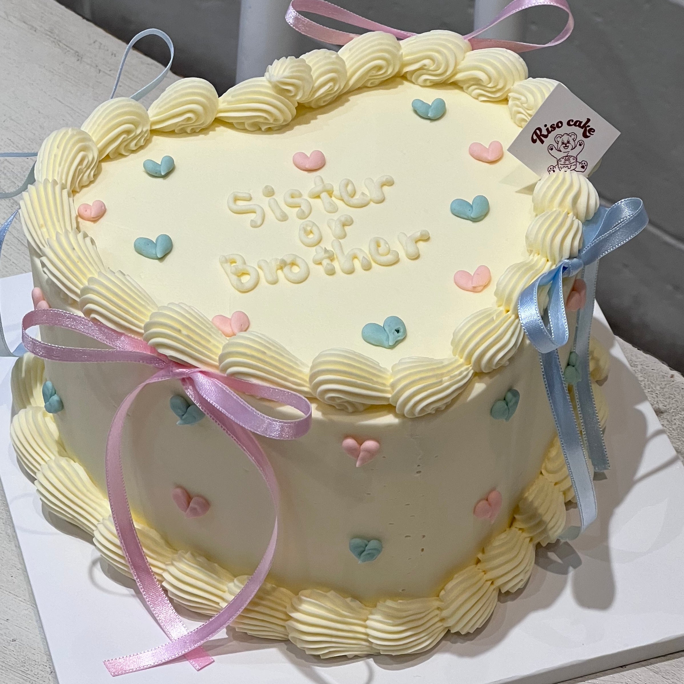 Soft pastel tones, heart sprinkles, and flowing ribbons make this cake the dreamiest way to reveal “Sister or Brother