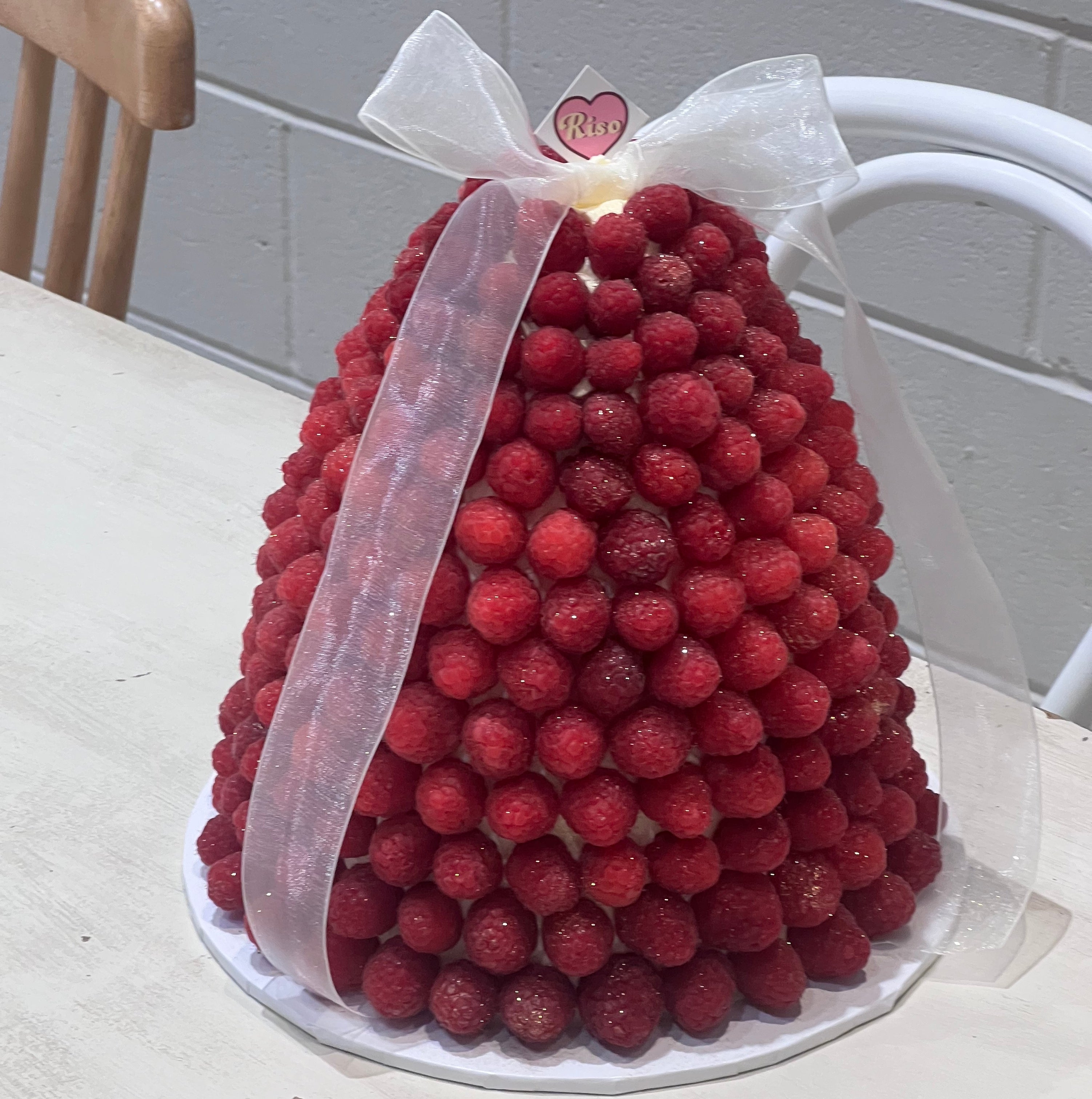 A raspberry-covered mountain-shaped cake with a white ribbon on top