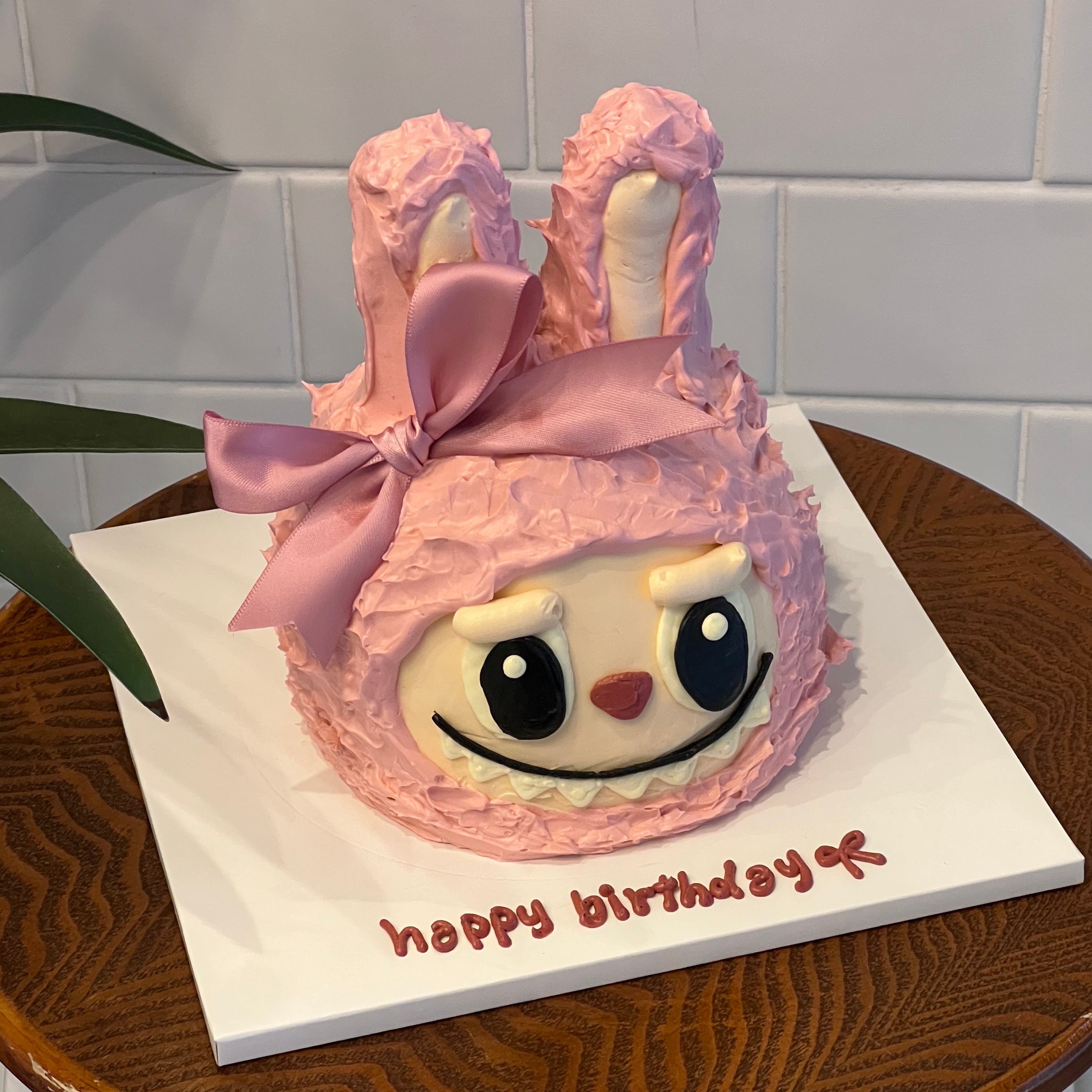 Close-up of pink Labubu cake with furry texture, big eyes, and a soft ribbon tied between two upright bunny ears