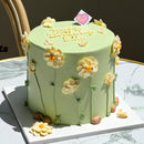 Round birthday cake with hand-piped white daisies on soft green frosting